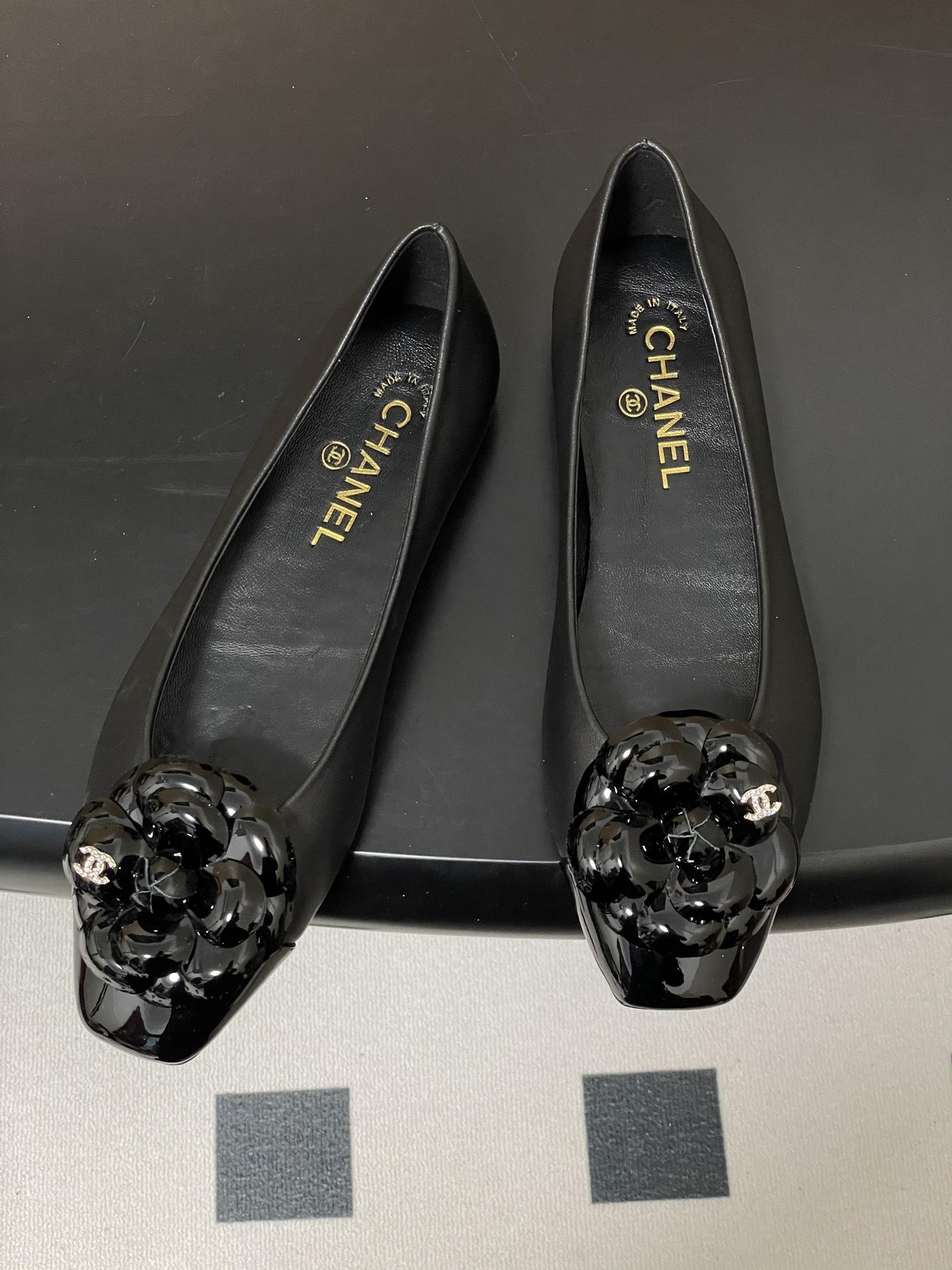 A pair of black Chanel ballet flats featuring a 3D camellia flower and patent leather square toe. - Hình 2