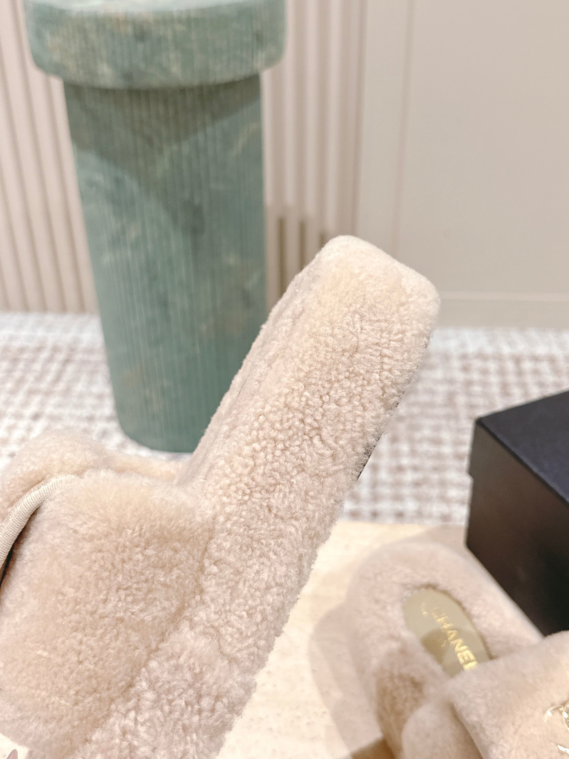 A pair of luxury beige Chanel shearling platform mules featuring gold CC logos on a stone pedestal. - Hình 8