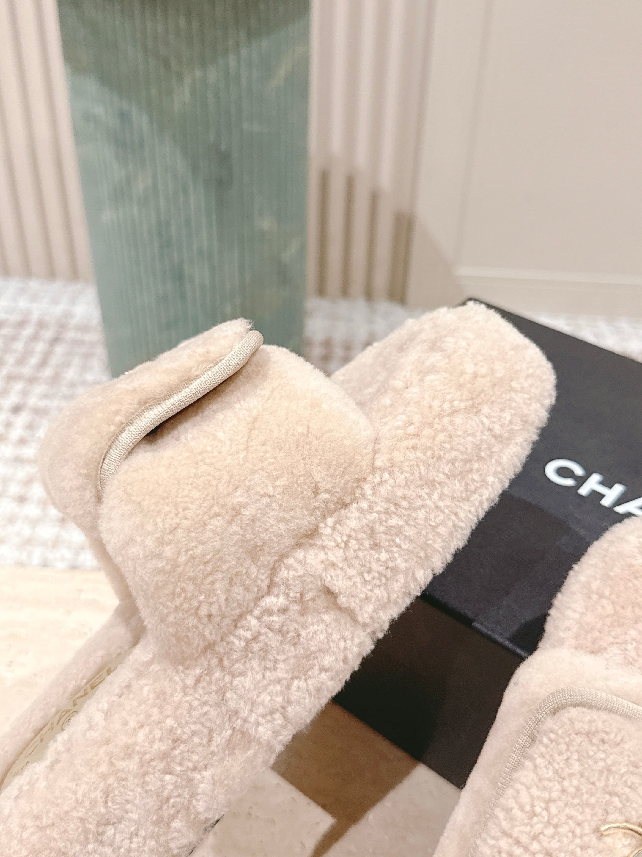 A pair of luxury beige Chanel shearling platform mules featuring gold CC logos on a stone pedestal. - Hình 6