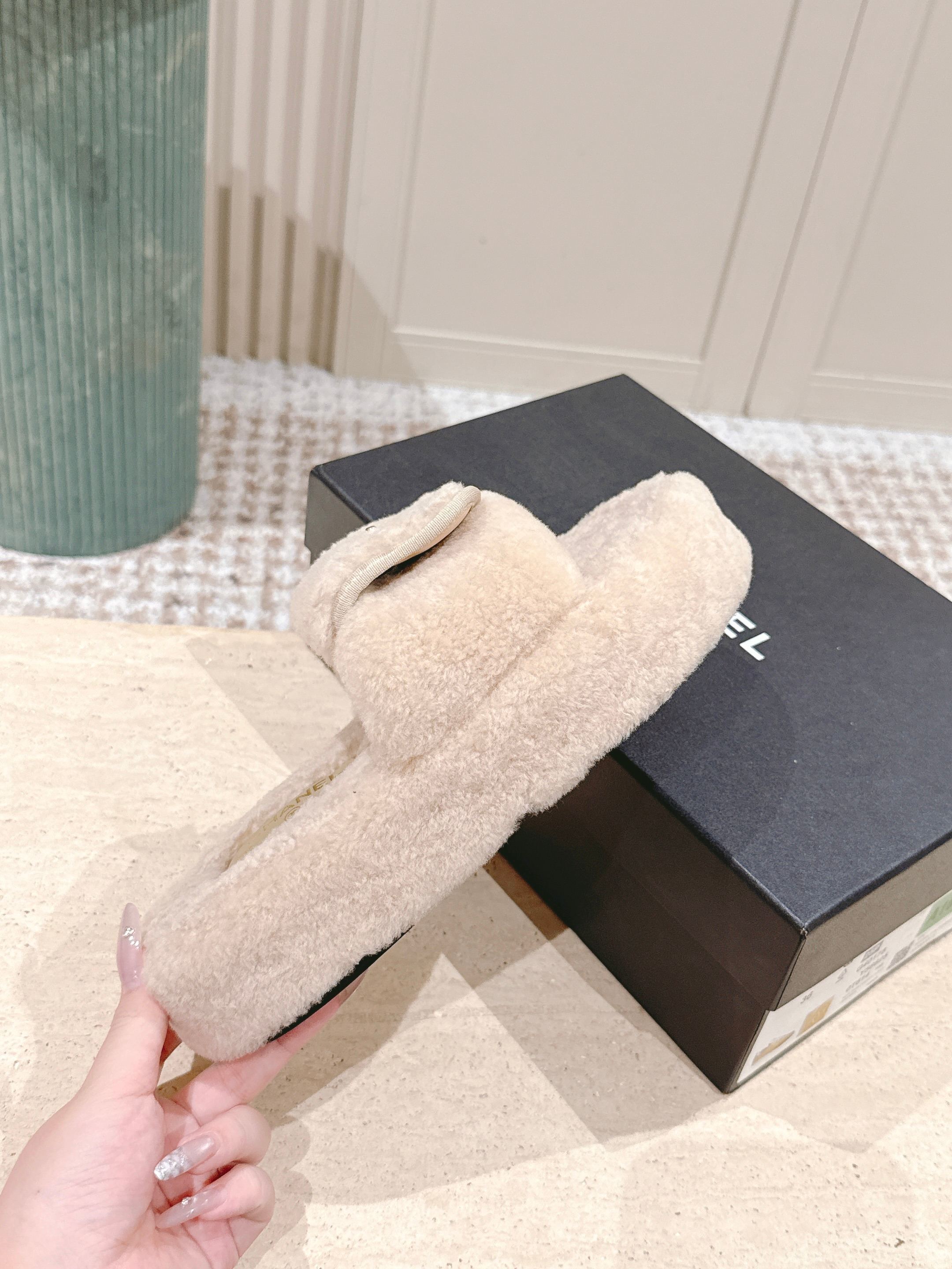 A pair of luxury beige Chanel shearling platform mules featuring gold CC logos on a stone pedestal. - Hình 5