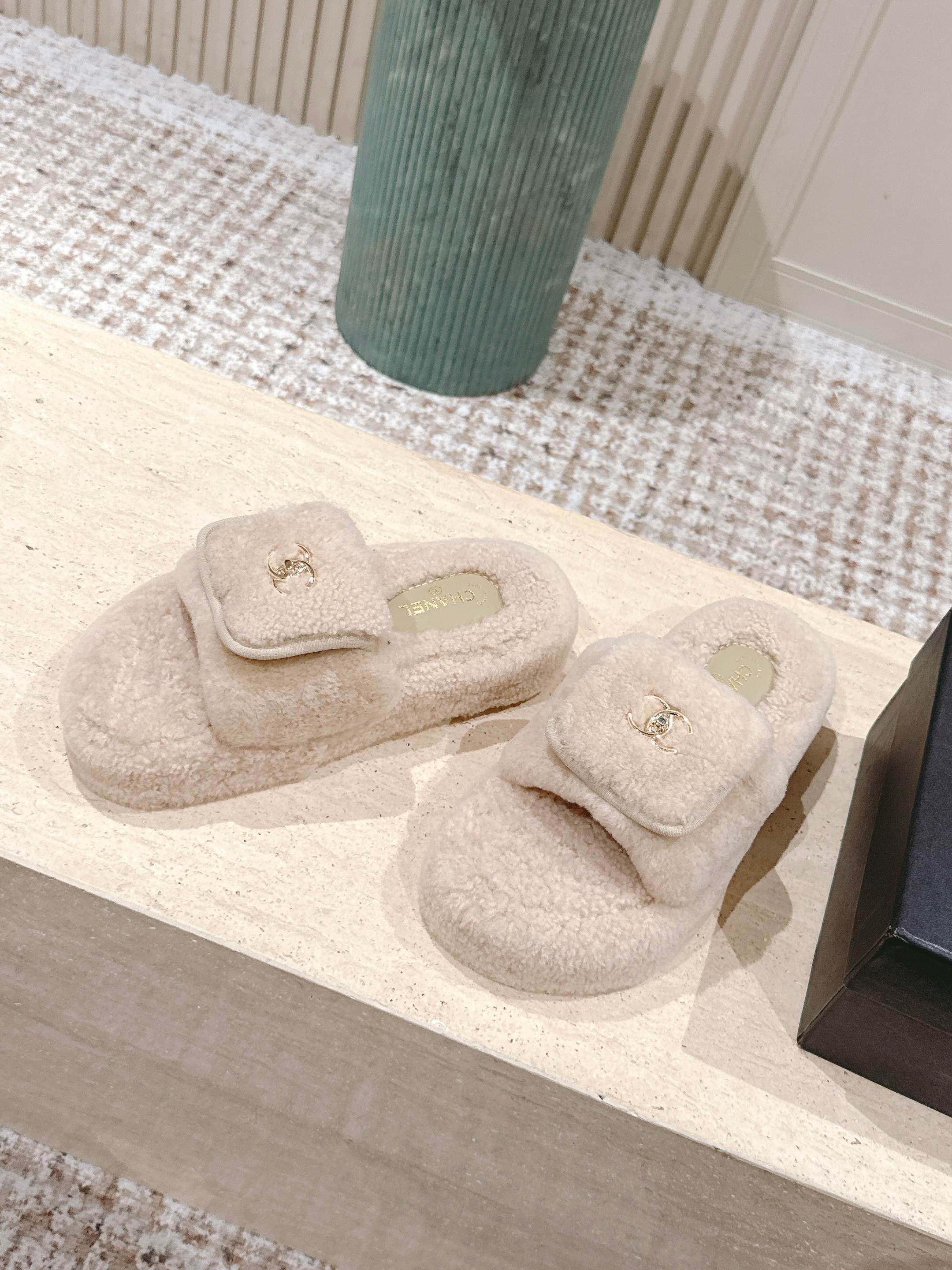 A pair of luxury beige Chanel shearling platform mules featuring gold CC logos on a stone pedestal. - Hình 3