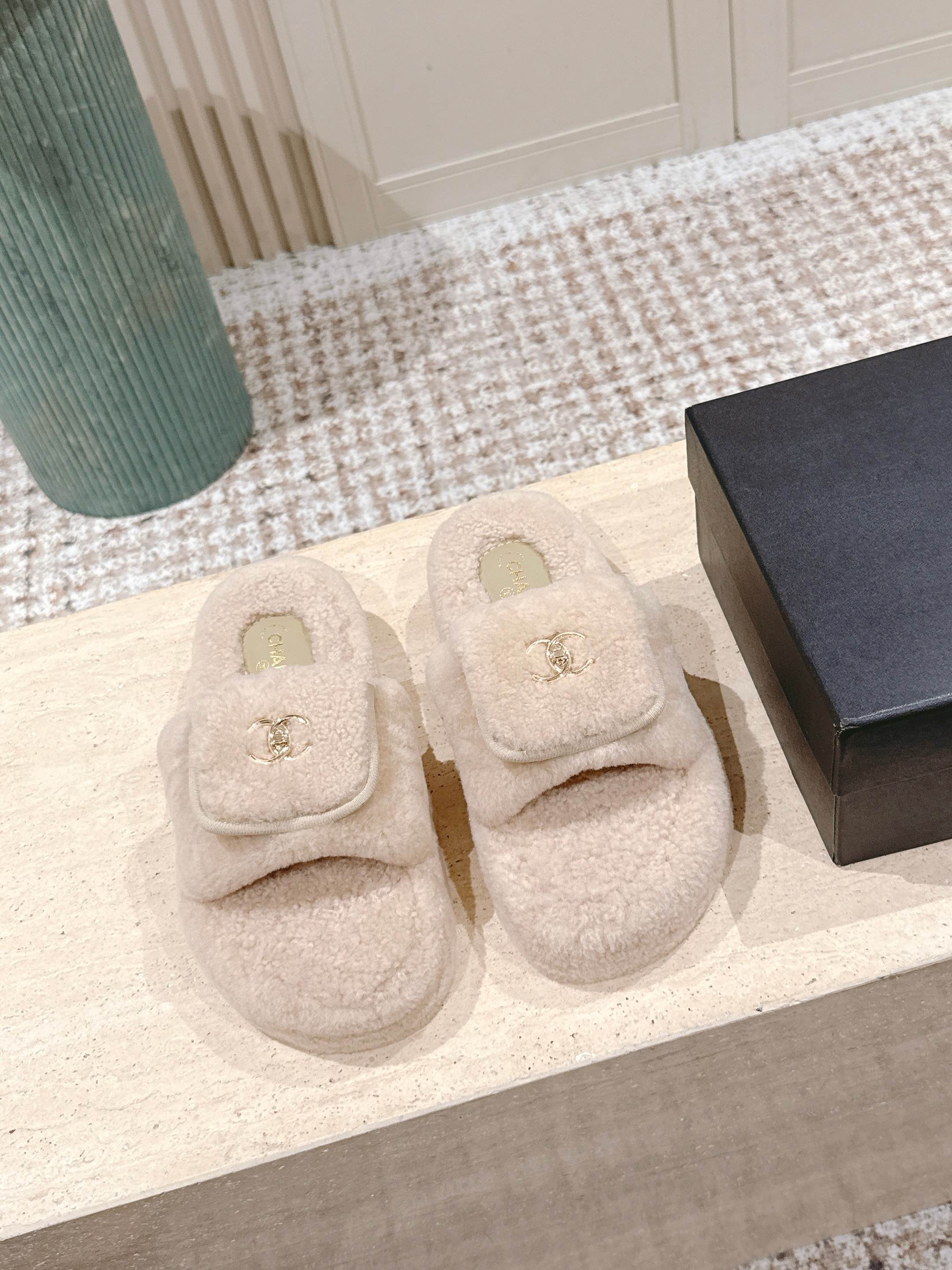 A pair of luxury beige Chanel shearling platform mules featuring gold CC logos on a stone pedestal. - Hình 2