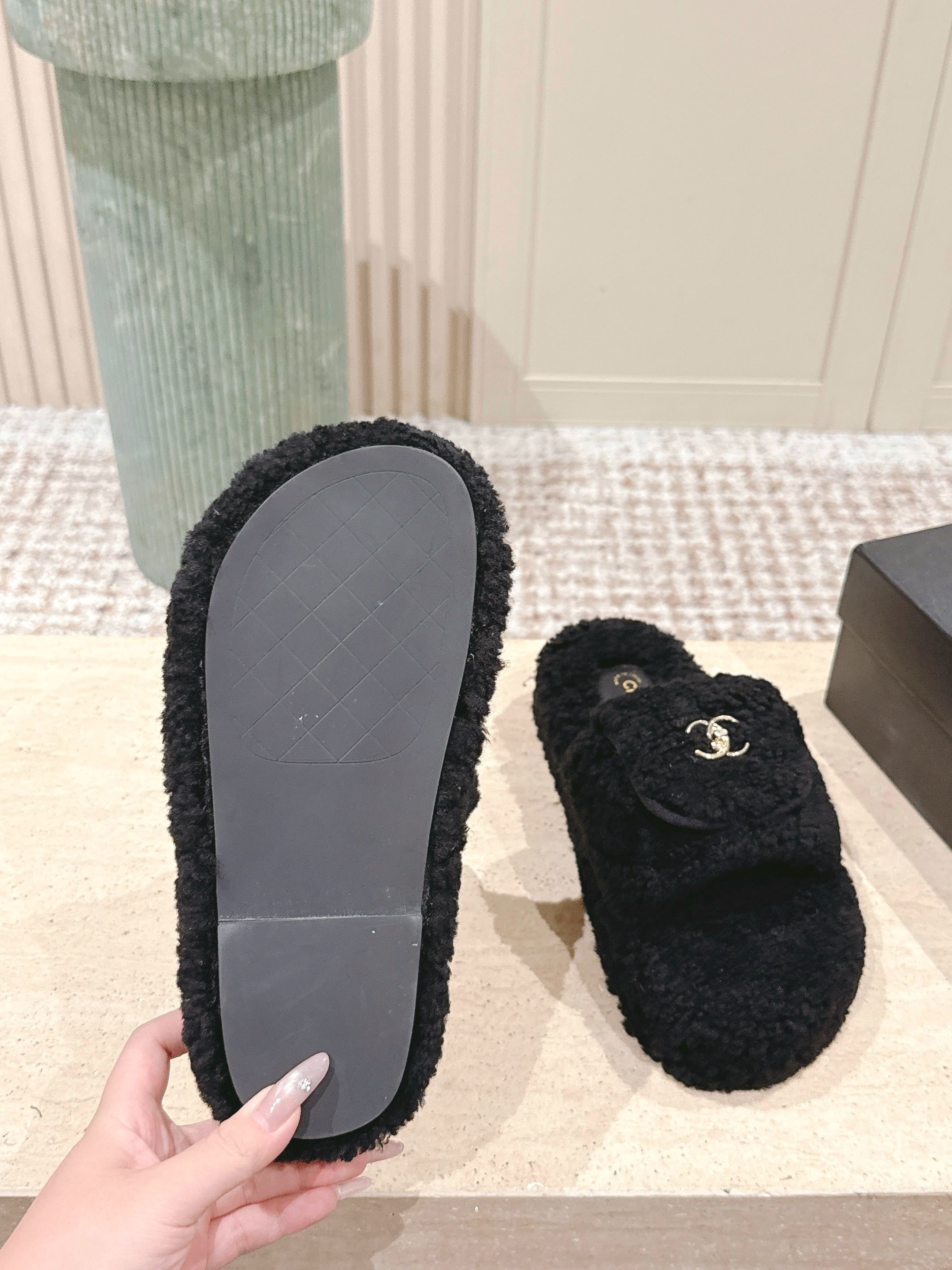 Luxury black Chanel shearling slides with gold CC logo displayed on a textured pedestal - Hình 9