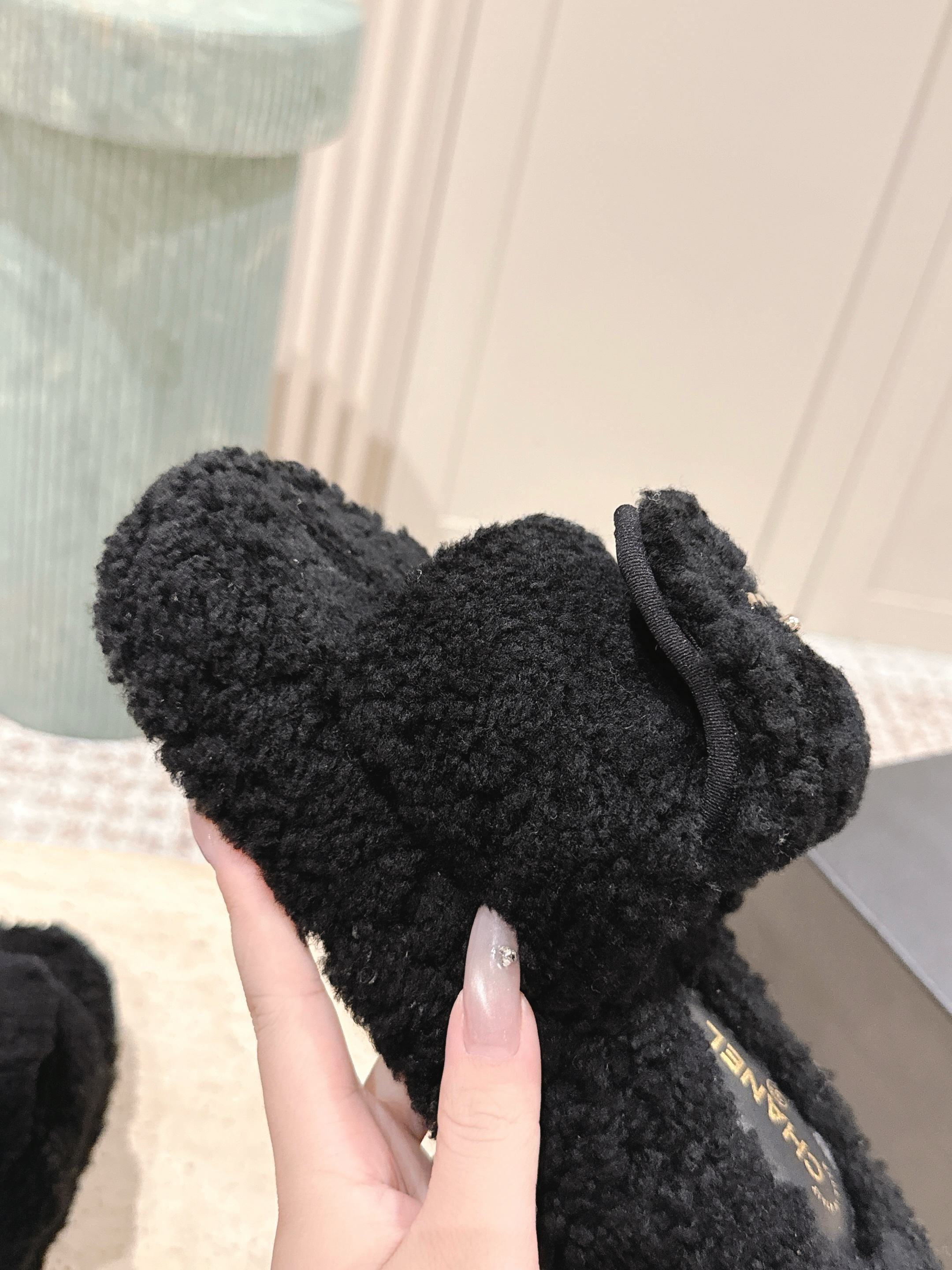 Luxury black Chanel shearling slides with gold CC logo displayed on a textured pedestal - Hình 6