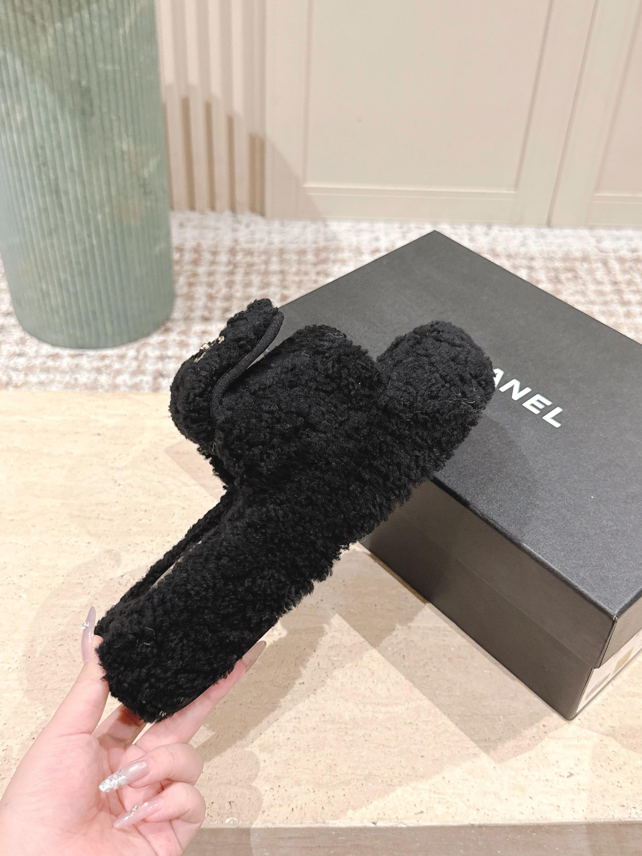 Luxury black Chanel shearling slides with gold CC logo displayed on a textured pedestal - Hình 4