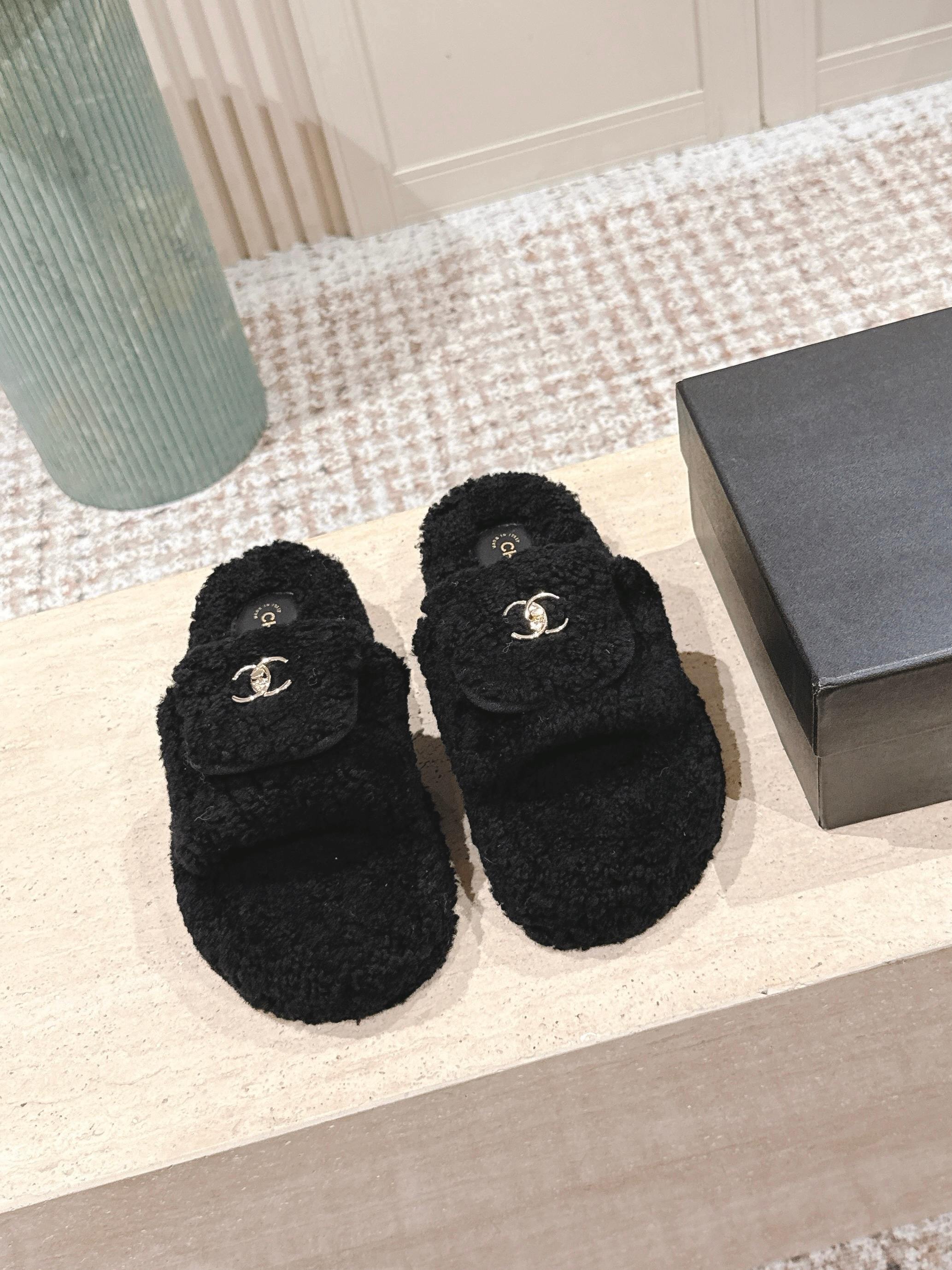 Luxury black Chanel shearling slides with gold CC logo displayed on a textured pedestal - Hình 2