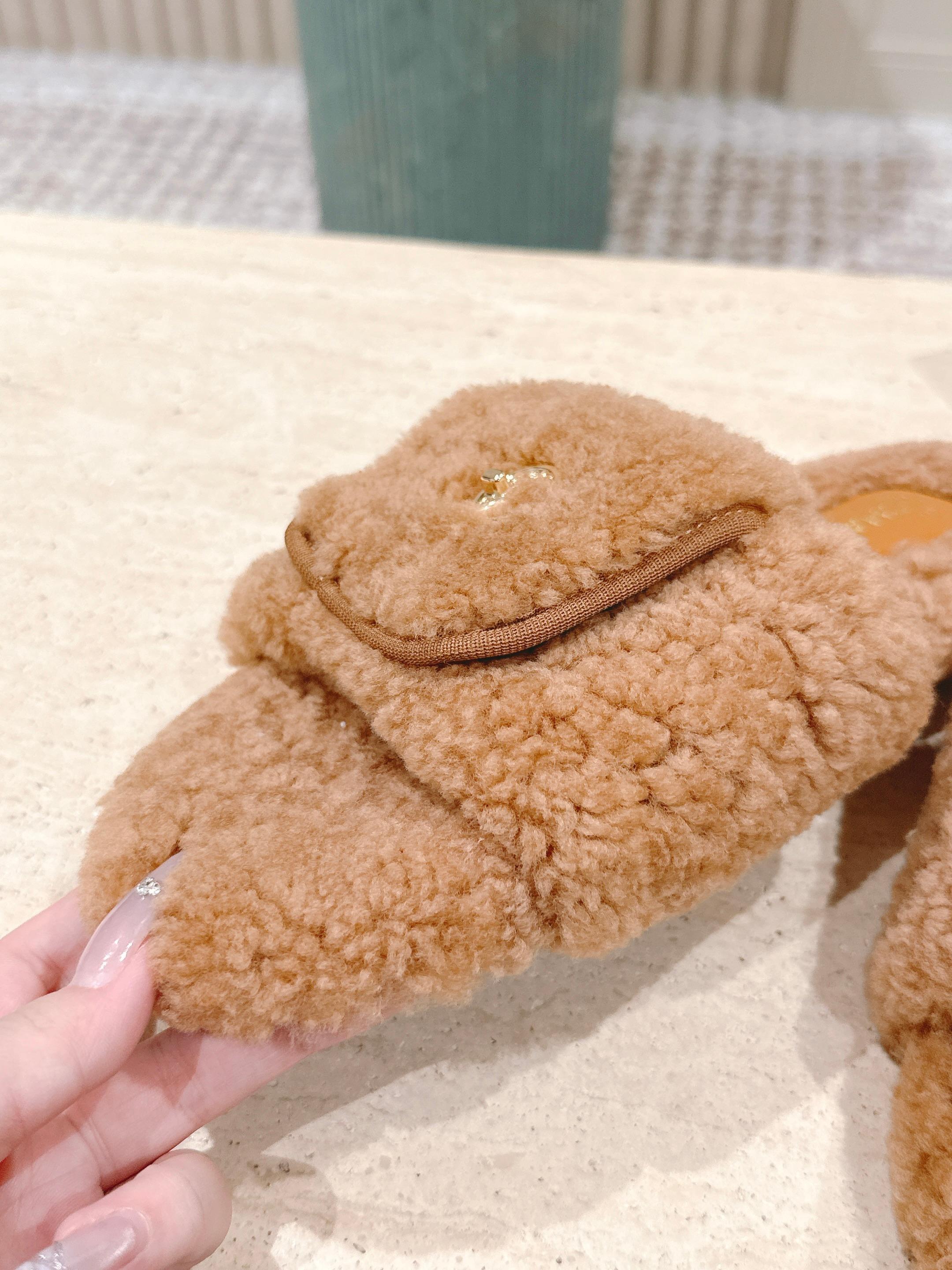 A pair of Chanel camel brown shearling slides featuring the gold CC logo on the strap, displayed on a marble countertop next to a black shoe box. - Hình 6