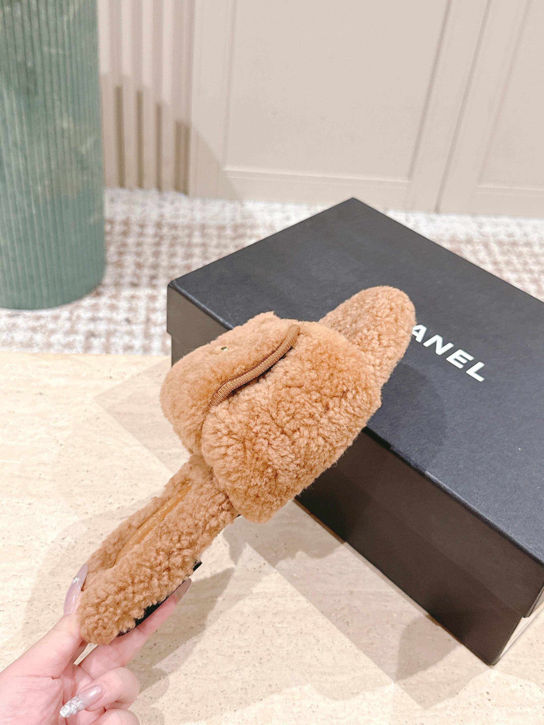 A pair of Chanel camel brown shearling slides featuring the gold CC logo on the strap, displayed on a marble countertop next to a black shoe box. - Hình 5