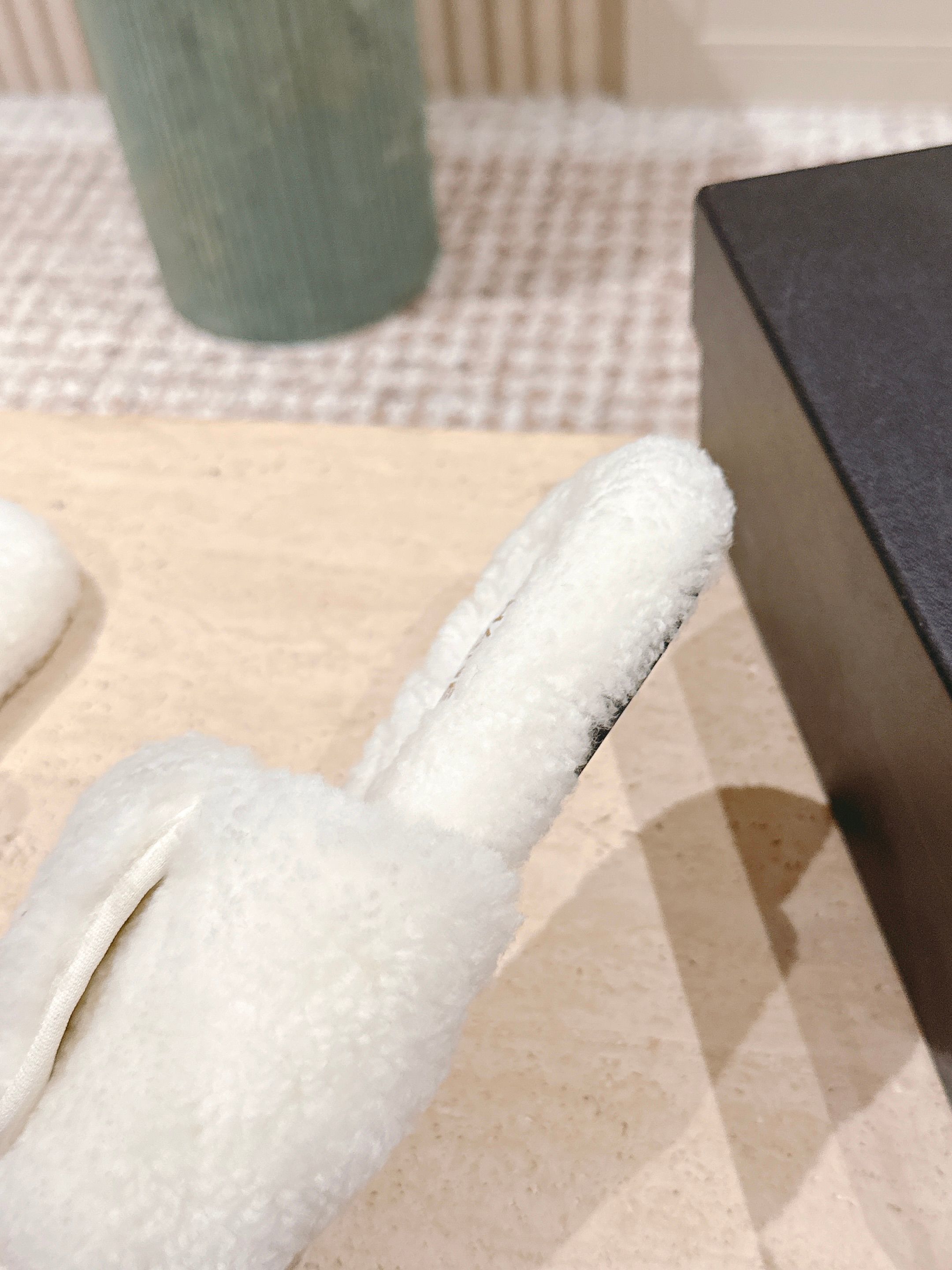 A pair of white Chanel shearling slides with gold CC logo displayed on a stone pedestal - Hình 8