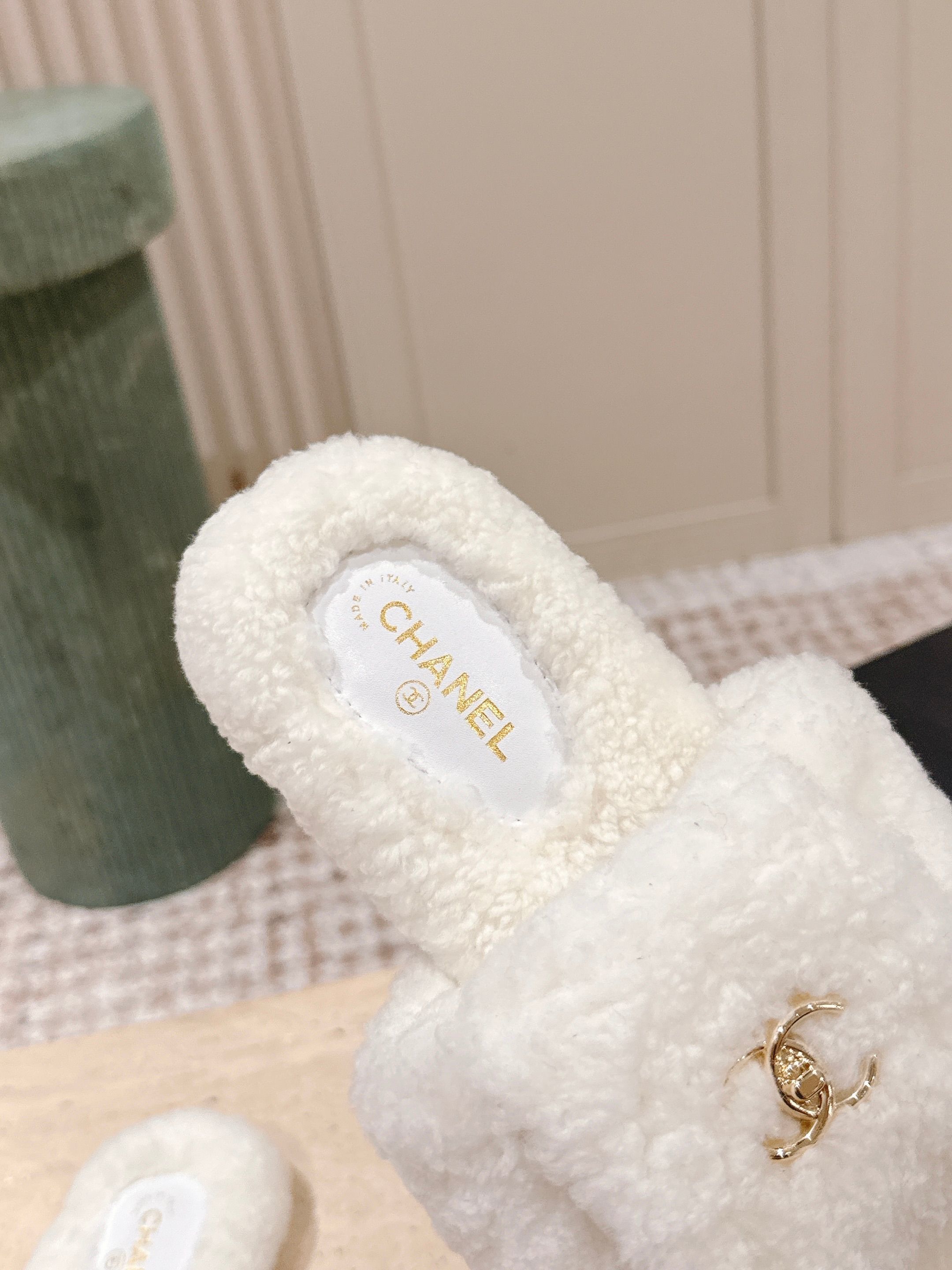 A pair of white Chanel shearling slides with gold CC logo displayed on a stone pedestal - Hình 7