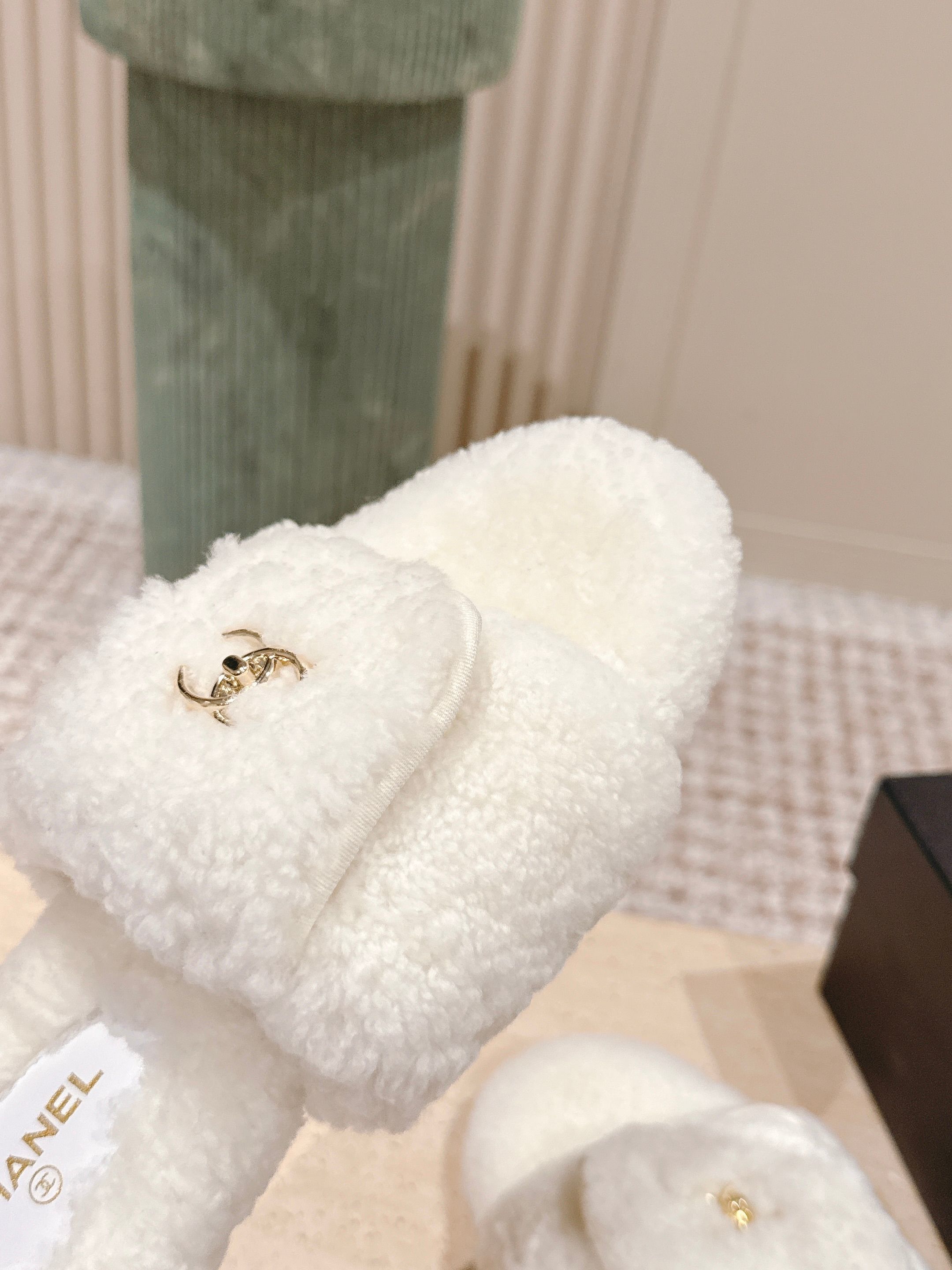 A pair of white Chanel shearling slides with gold CC logo displayed on a stone pedestal - Hình 6