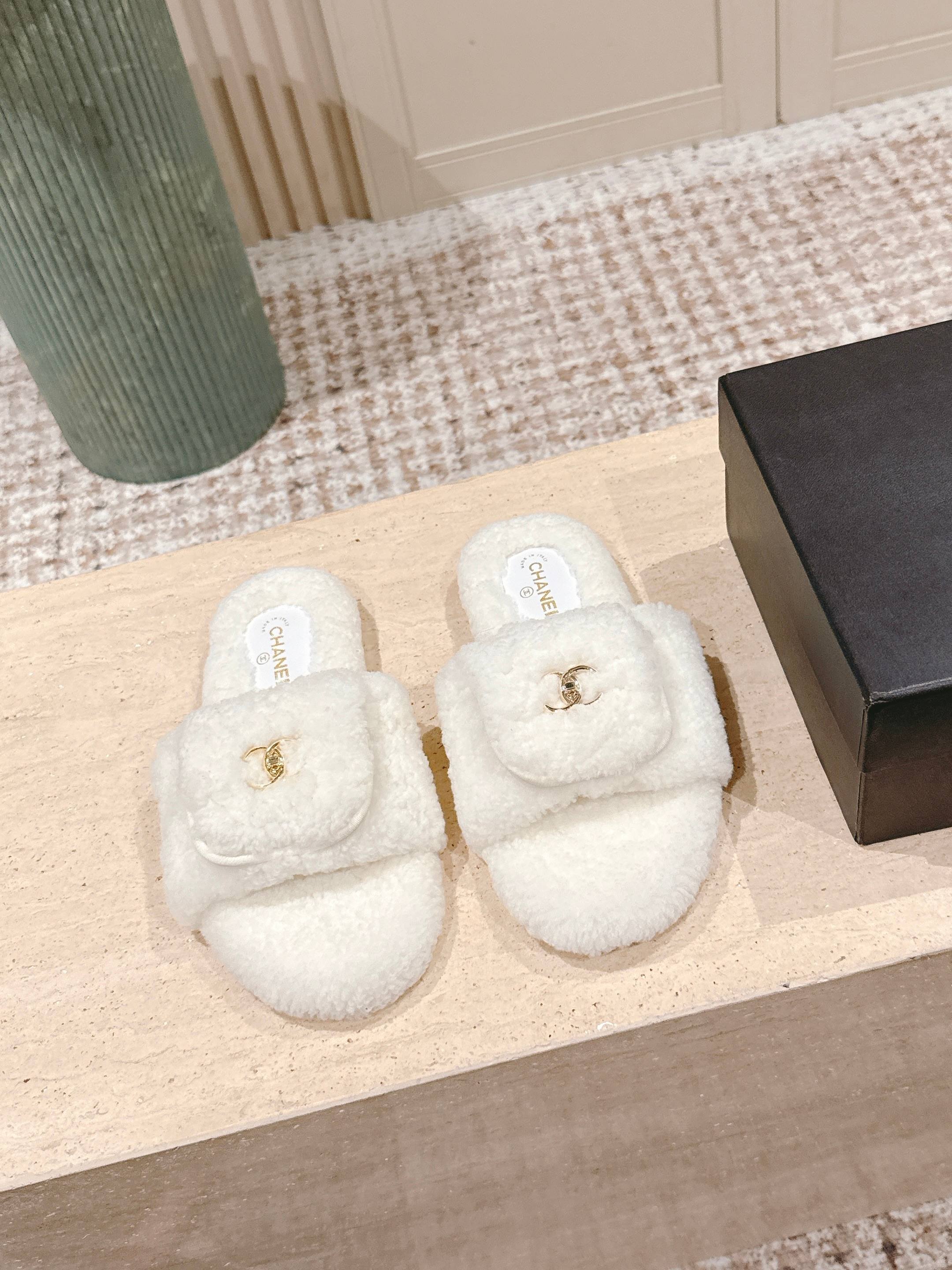 A pair of white Chanel shearling slides with gold CC logo displayed on a stone pedestal - Hình 2