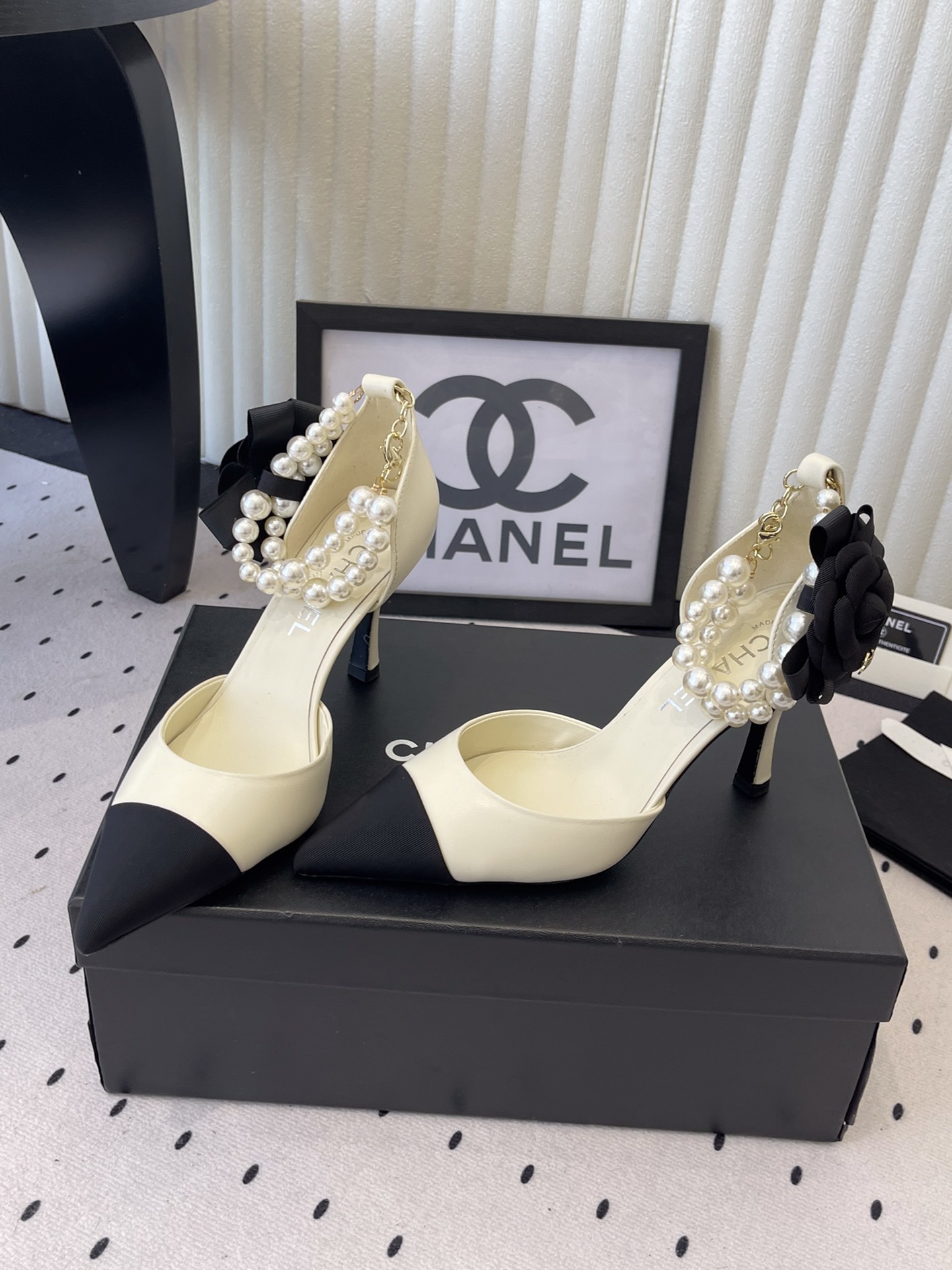 Luxury Chanel cream pumps with black pointed toes, featuring a pearl ankle strap and a black camellia flower detail with CC logo. - Hình 9