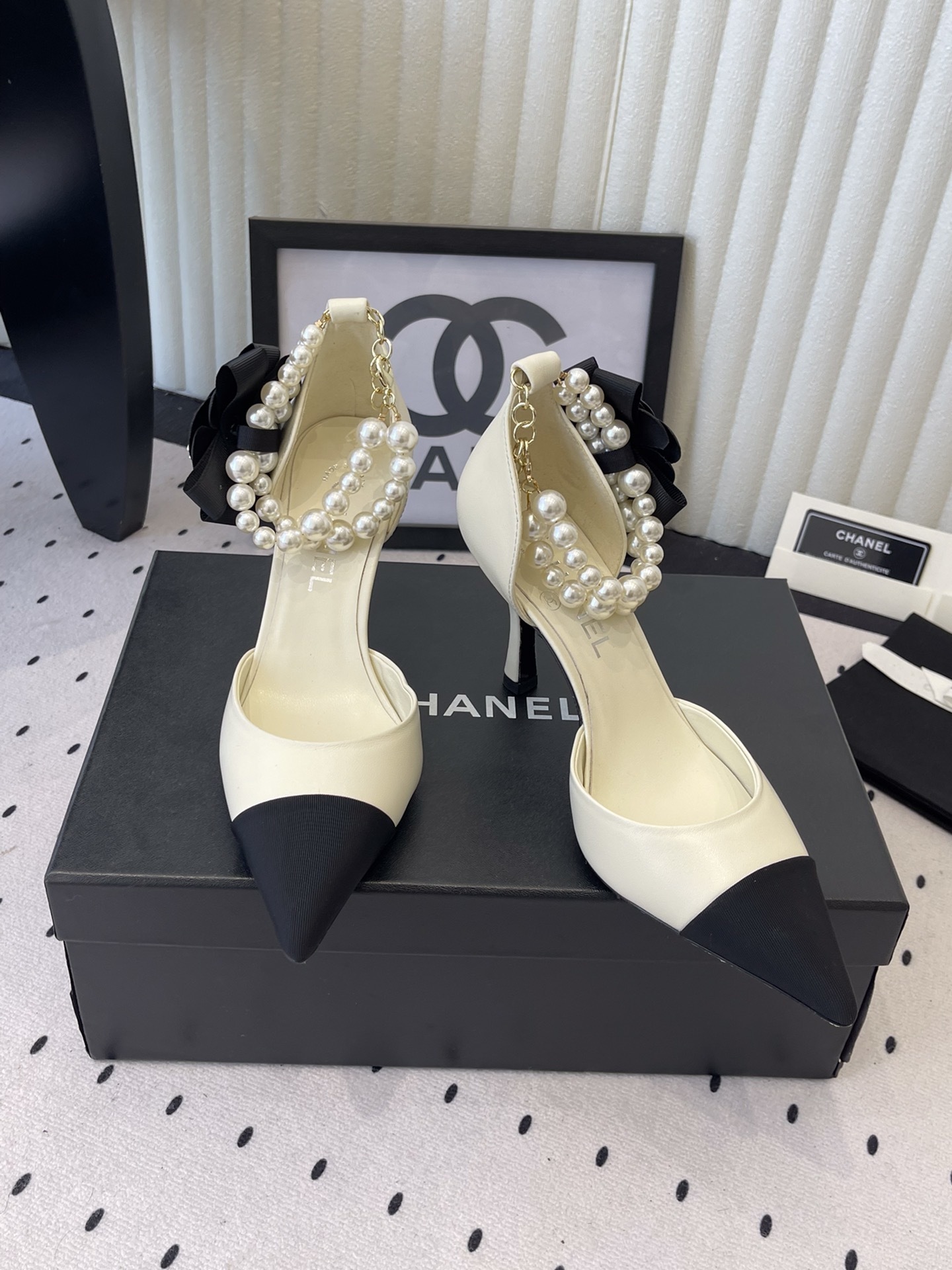 Luxury Chanel cream pumps with black pointed toes, featuring a pearl ankle strap and a black camellia flower detail with CC logo. - Hình 8