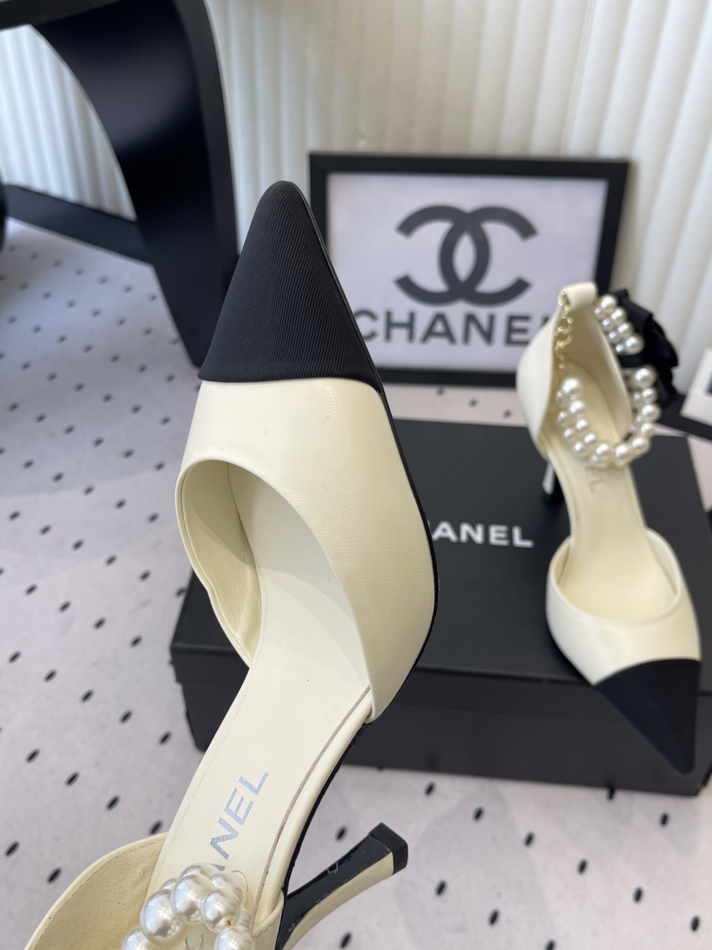 Luxury Chanel cream pumps with black pointed toes, featuring a pearl ankle strap and a black camellia flower detail with CC logo. - Hình 7