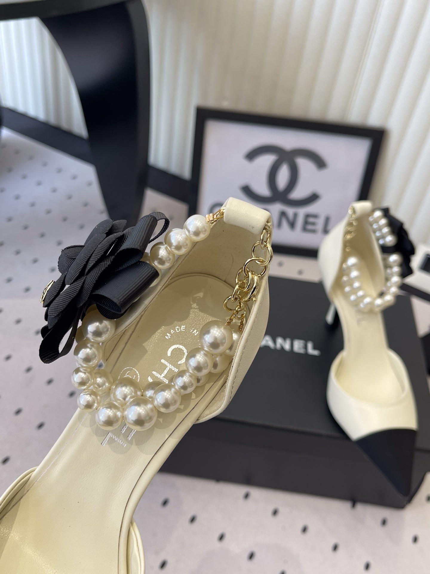 Luxury Chanel cream pumps with black pointed toes, featuring a pearl ankle strap and a black camellia flower detail with CC logo. - Hình 6