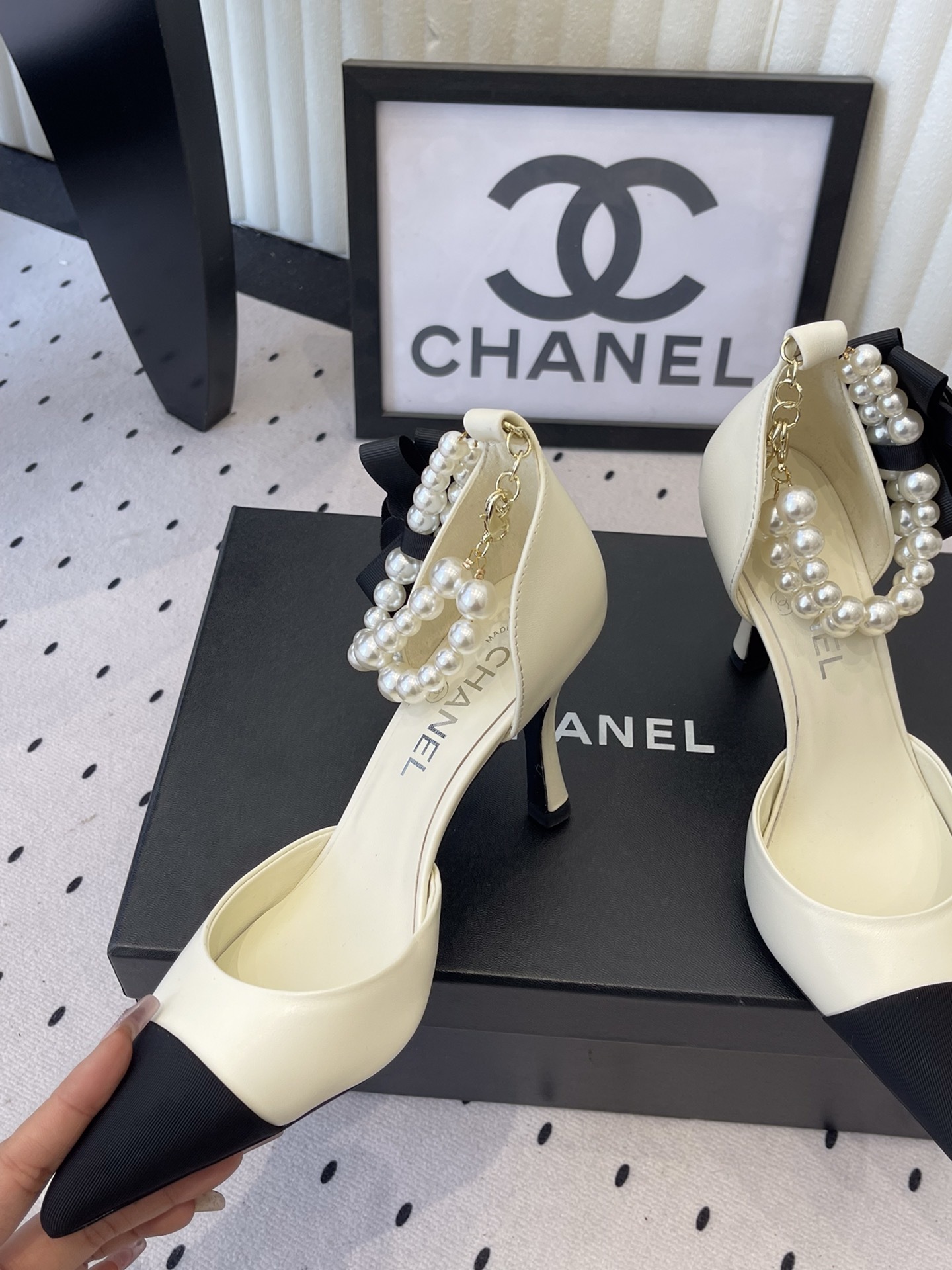 Luxury Chanel cream pumps with black pointed toes, featuring a pearl ankle strap and a black camellia flower detail with CC logo. - Hình 5