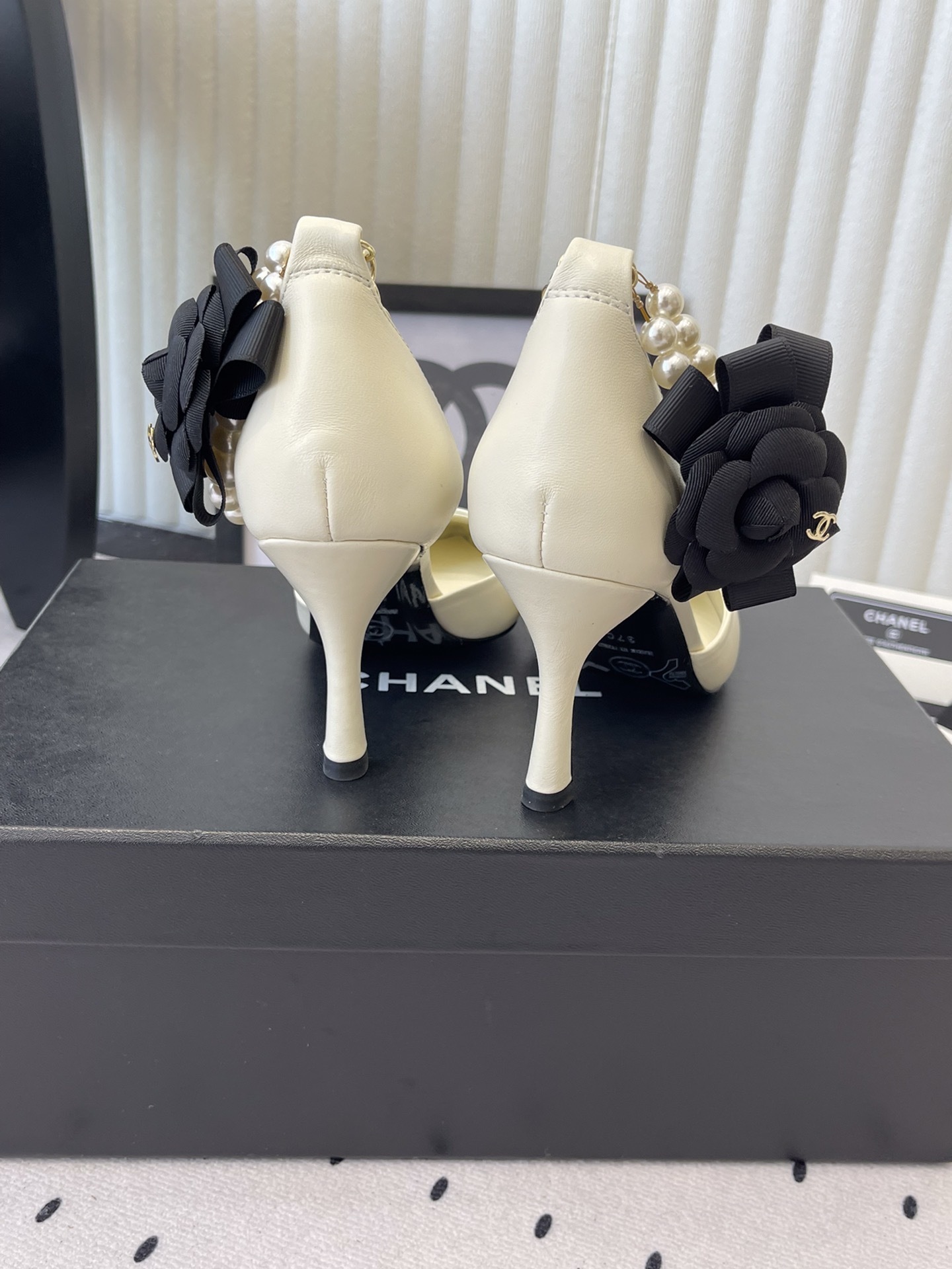 Luxury Chanel cream pumps with black pointed toes, featuring a pearl ankle strap and a black camellia flower detail with CC logo. - Hình 3