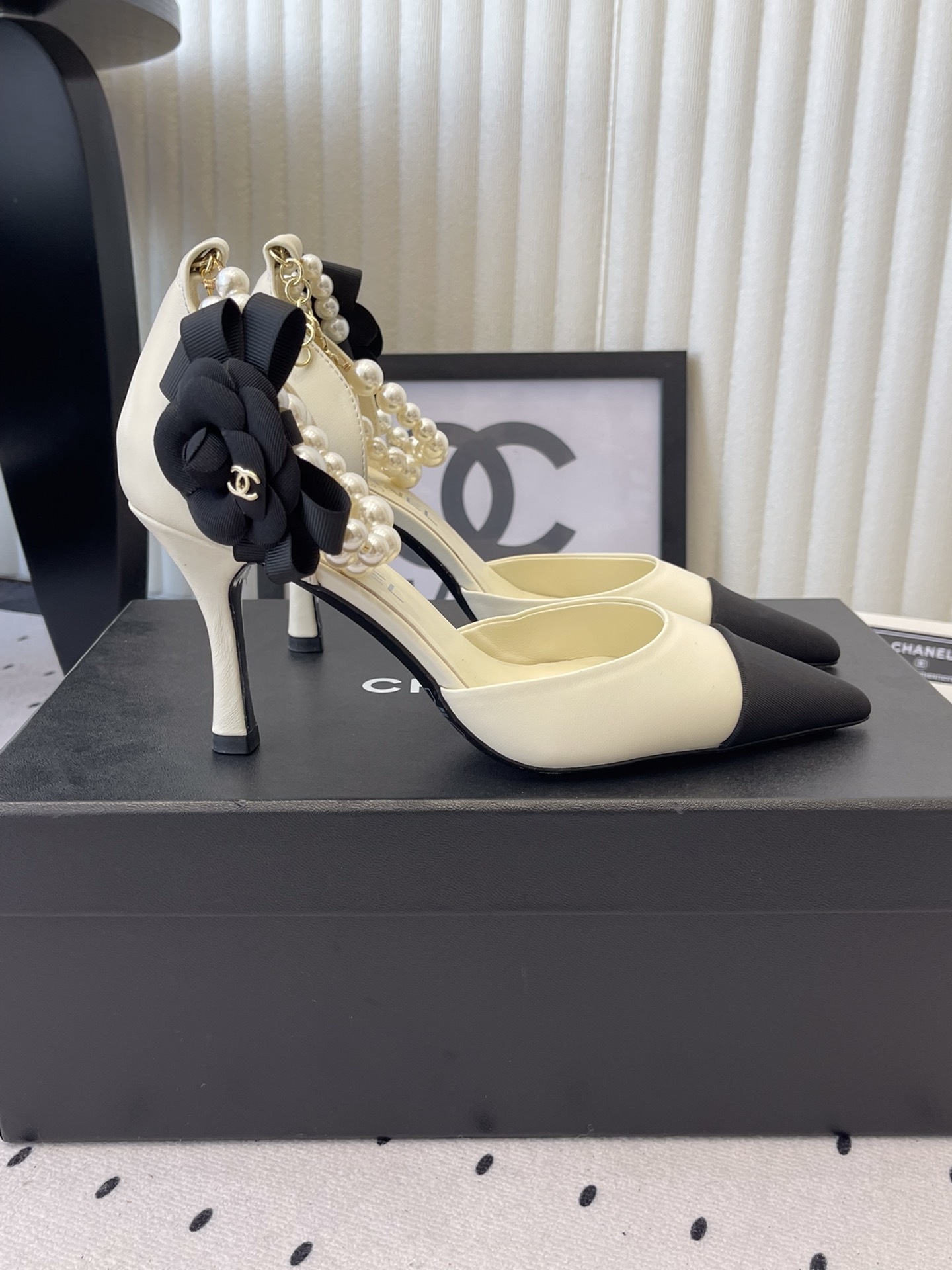 Luxury Chanel cream pumps with black pointed toes, featuring a pearl ankle strap and a black camellia flower detail with CC logo. - Hình 2