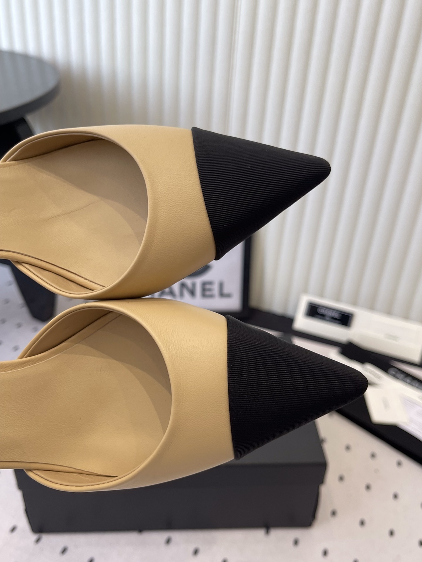 Luxury beige and black two-tone pointed-toe pumps with pearl ankle strap and black camellia flower detail on a designer box. - Hình 4