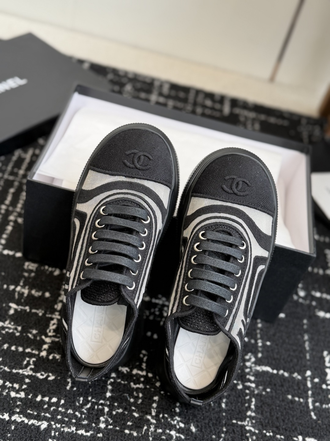 Pair of Chanel black and white knit sneakers with CC logo on toe and chunky black soles sitting on a luxury shoe box. - Hình 4