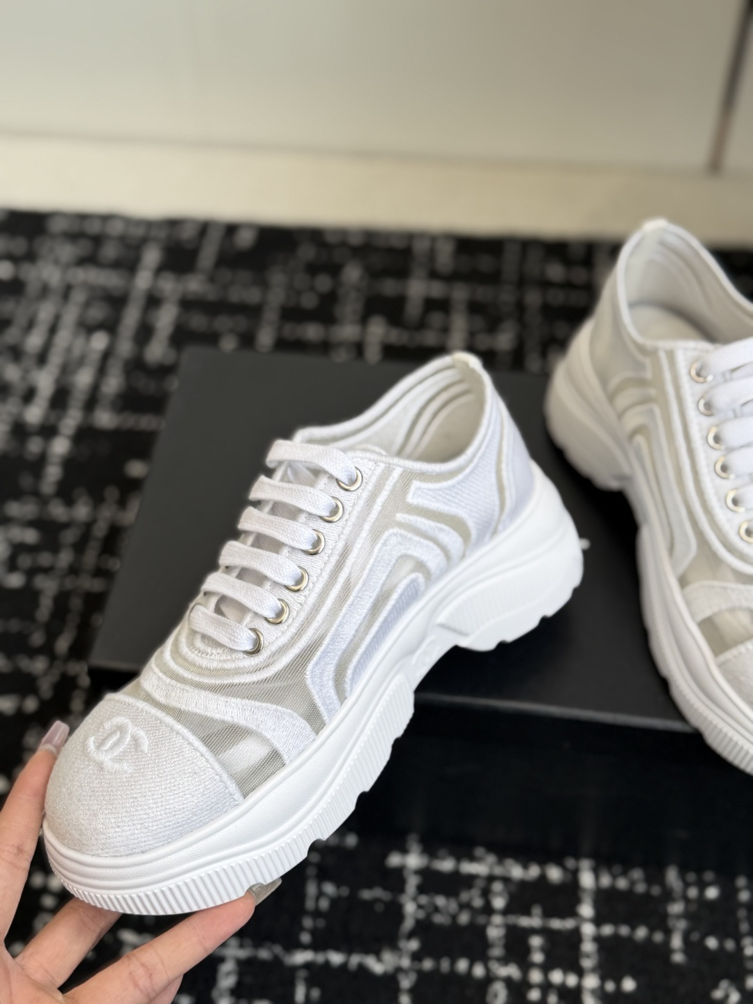 A pair of luxury Chanel white mesh and fabric sneakers with chunky soles and CC logo detail displayed on a black box. - Hình 6