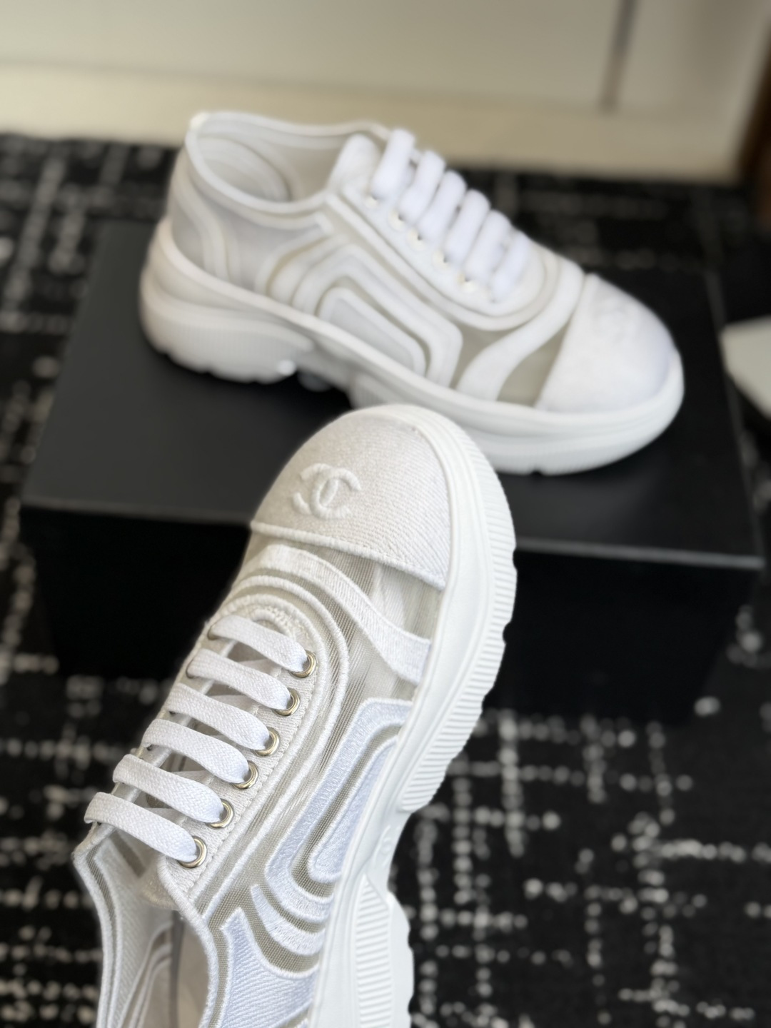 A pair of luxury Chanel white mesh and fabric sneakers with chunky soles and CC logo detail displayed on a black box. - Hình 5