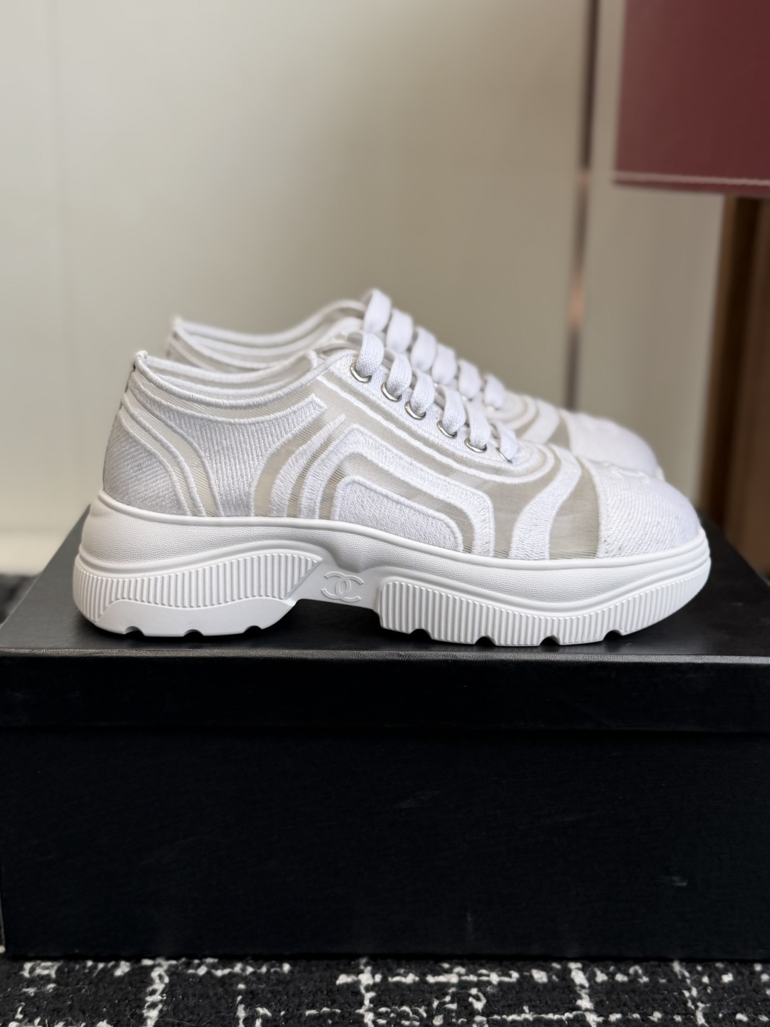 A pair of luxury Chanel white mesh and fabric sneakers with chunky soles and CC logo detail displayed on a black box. - Hình 2