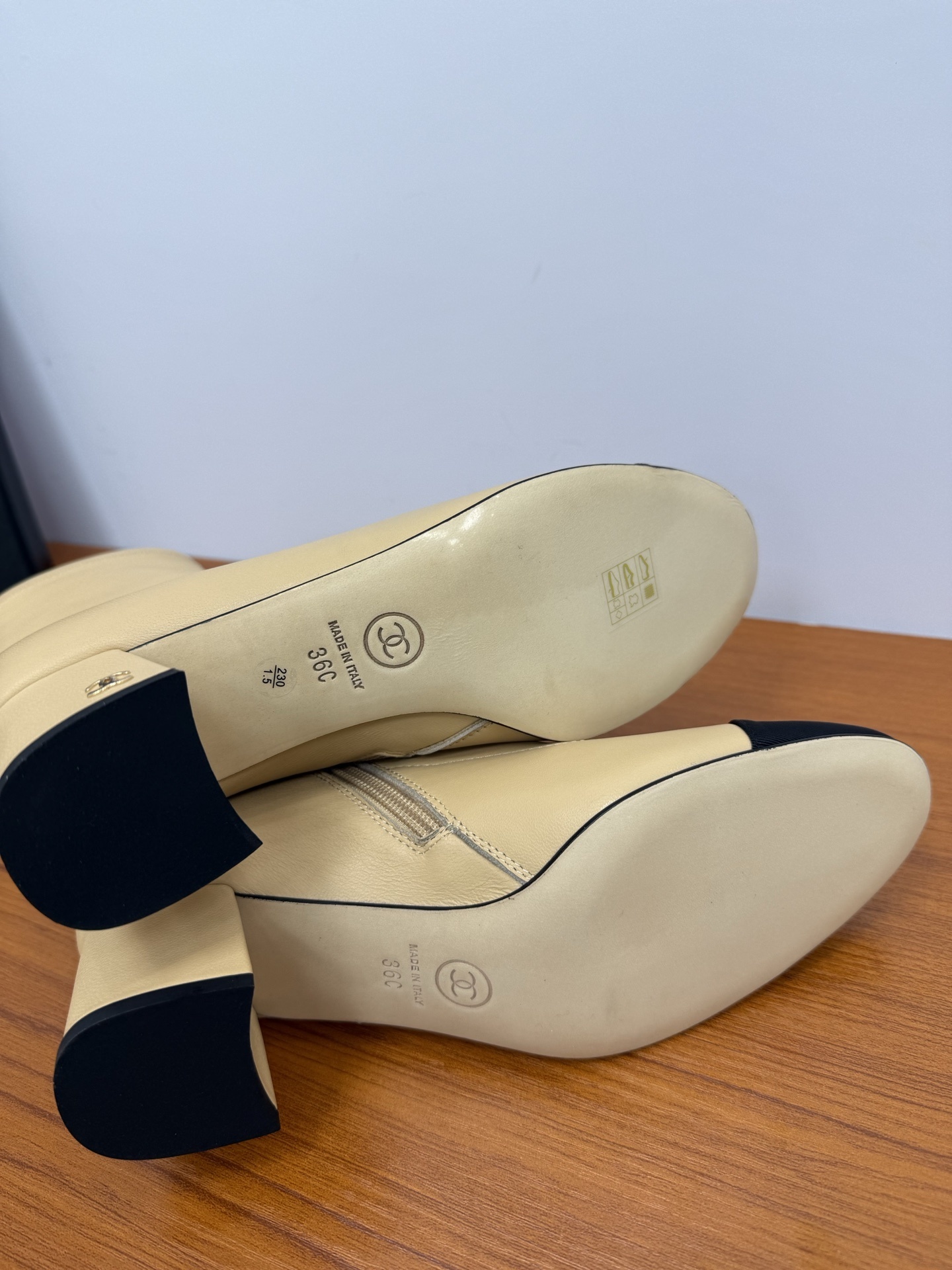 A pair of elegant beige leather-look ankle boots with a black cap toe and a sturdy block heel on a wooden surface. - Hình 9