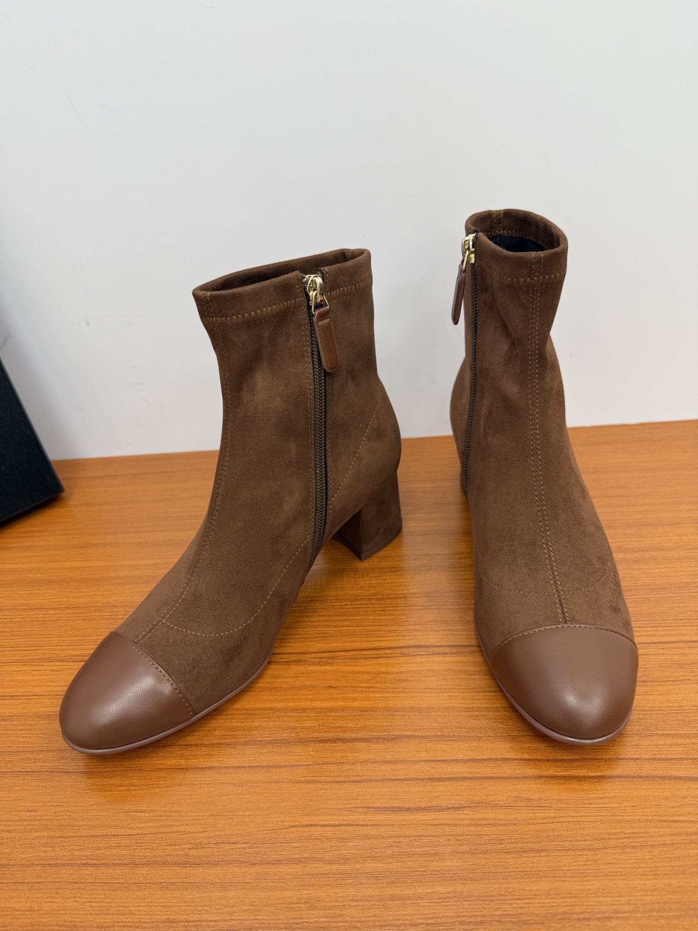 A pair of stylish brown suede ankle boots with a smooth leather cap-toe and block heels displayed on a wooden surface. - Hình 6