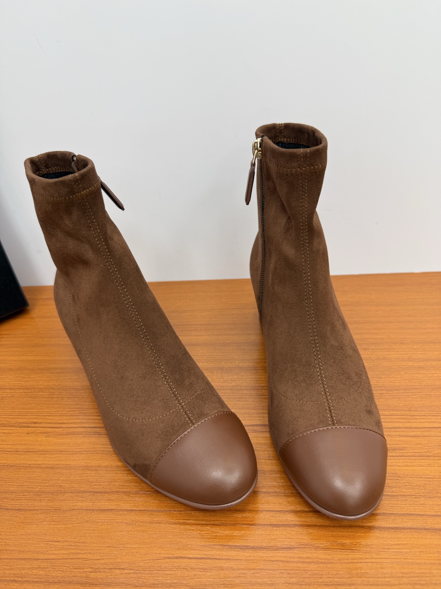 A pair of stylish brown suede ankle boots with a smooth leather cap-toe and block heels displayed on a wooden surface. - Hình 4