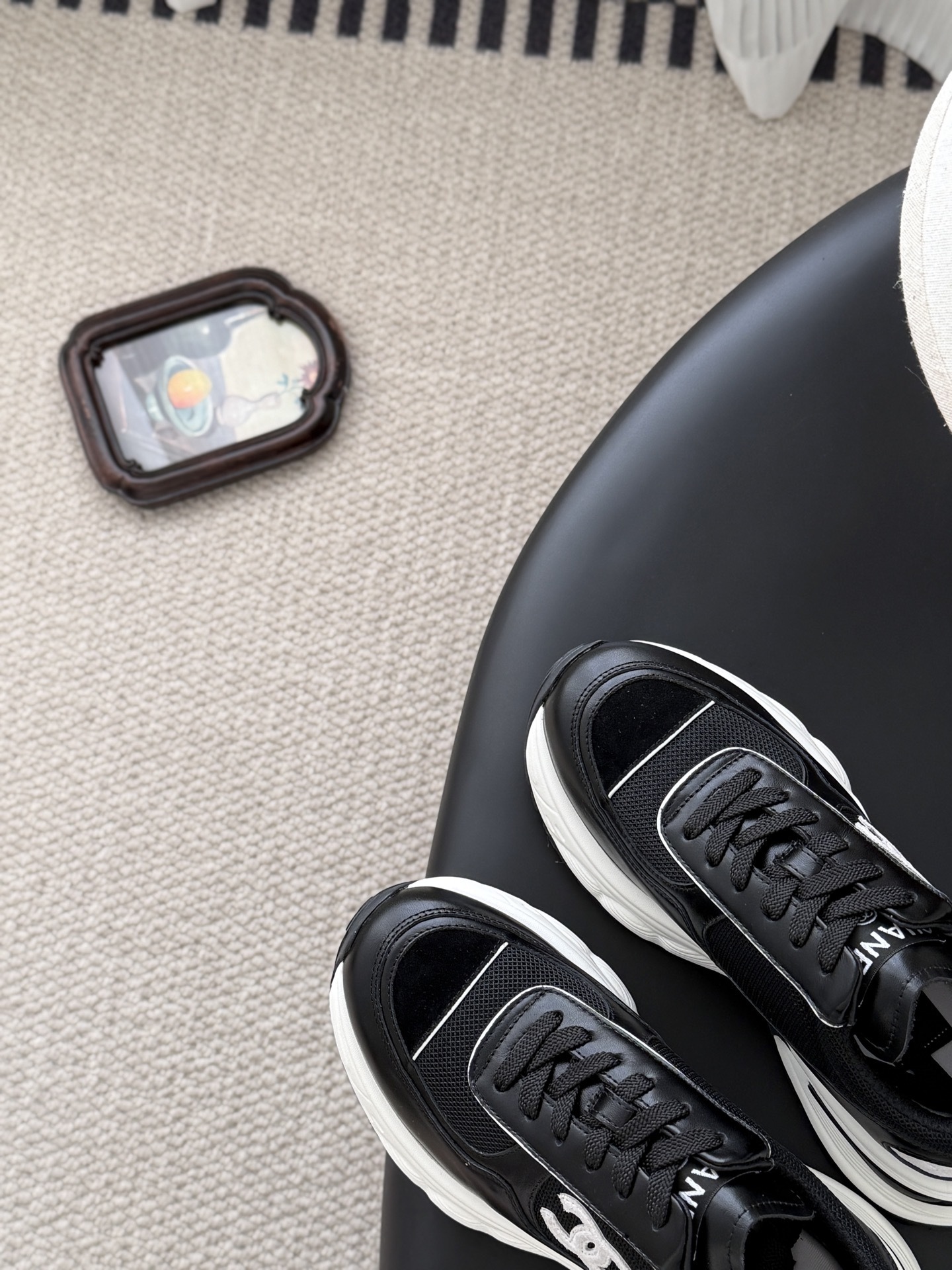 A pair of black and white Chanel chunky leather sneakers featuring the signature CC logo on a black surface next to a branded box. - Hình 7