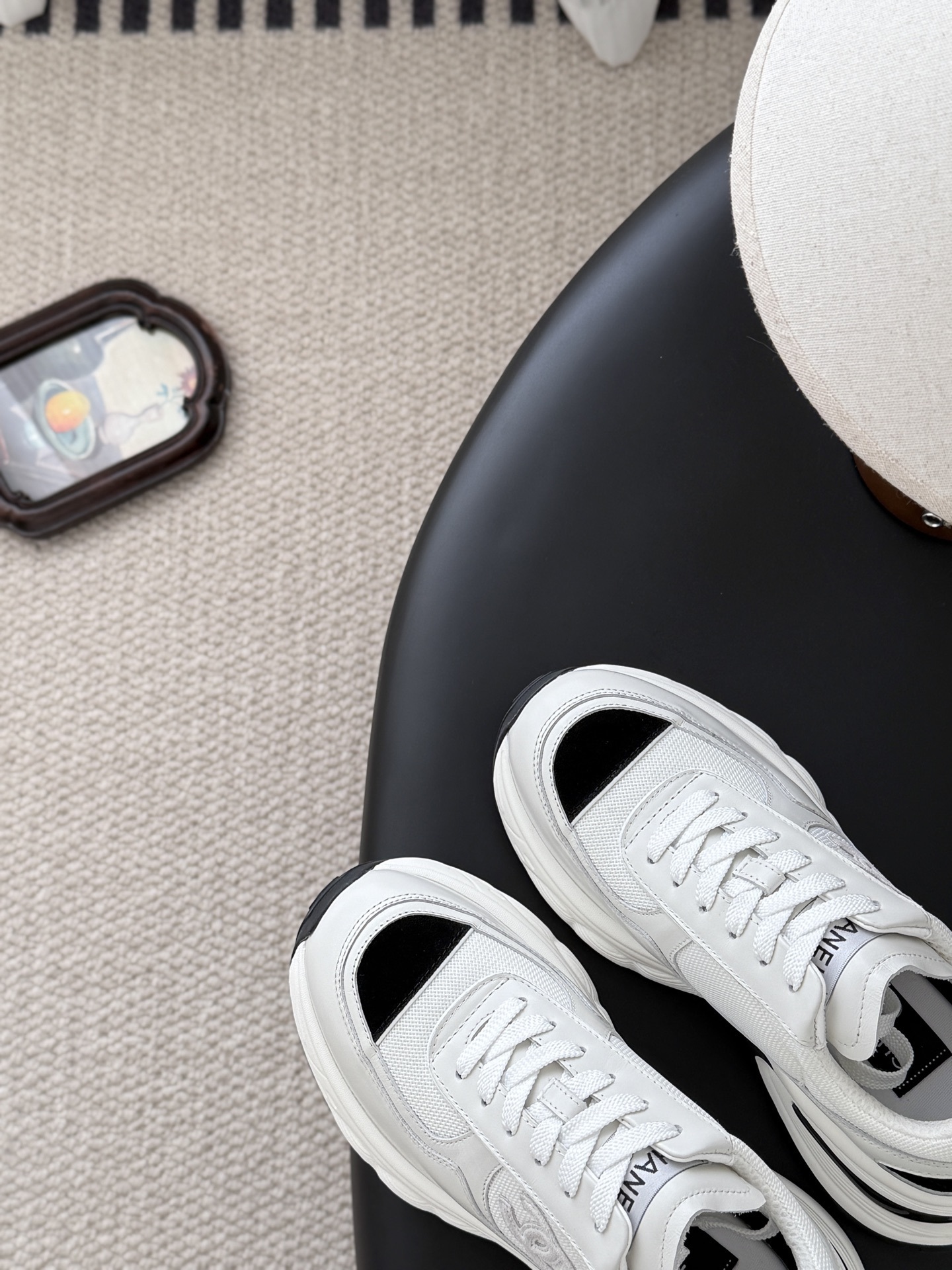 A pair of Chanel white chunky sneakers with black accents and interlocking CC logo displayed on a black surface next to a Chanel shoe box. - Hình 7