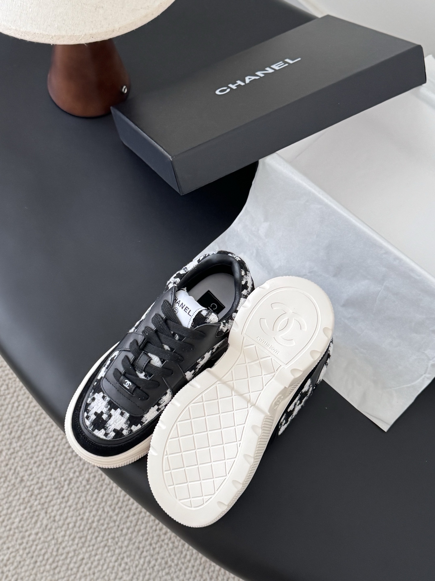 A pair of Chanel black and white houndstooth tweed sneakers with chunky white soles displayed next to a Chanel shoe box. - Hình 5