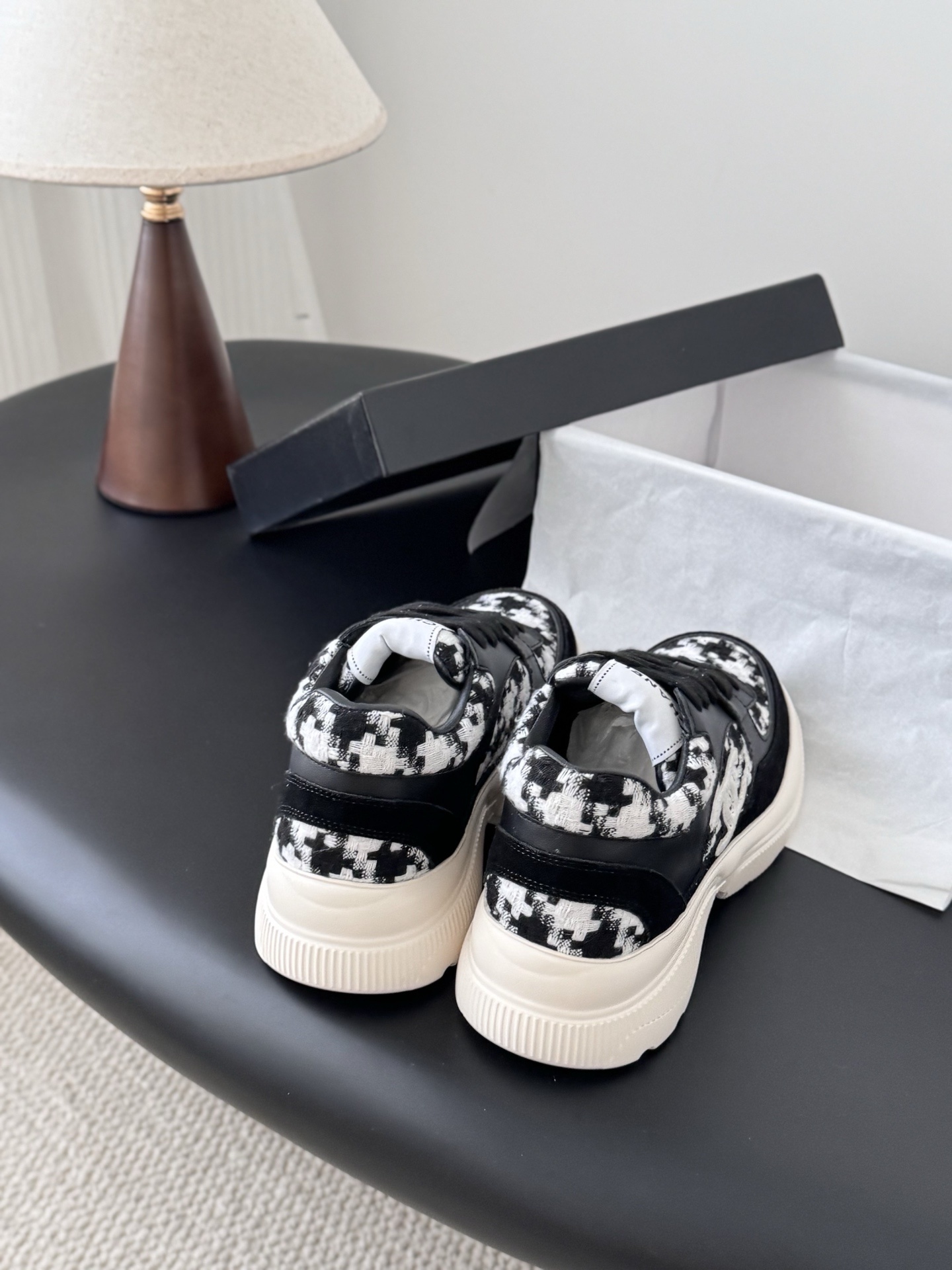A pair of Chanel black and white houndstooth tweed sneakers with chunky white soles displayed next to a Chanel shoe box. - Hình 3