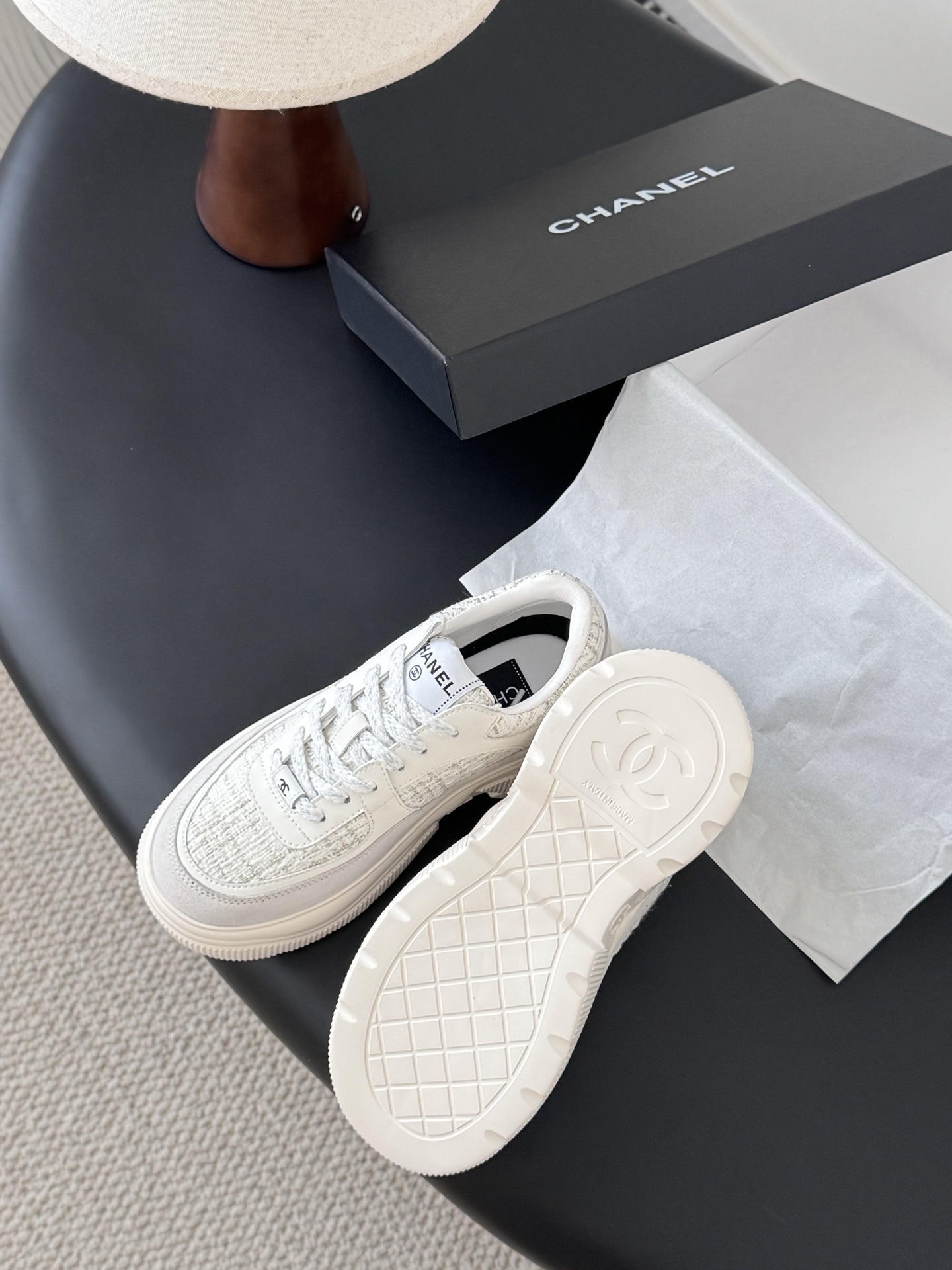A pair of white Chanel sneakers featuring tweed panels and leather overlays presented next to an original black Chanel brand box. - Hình 5