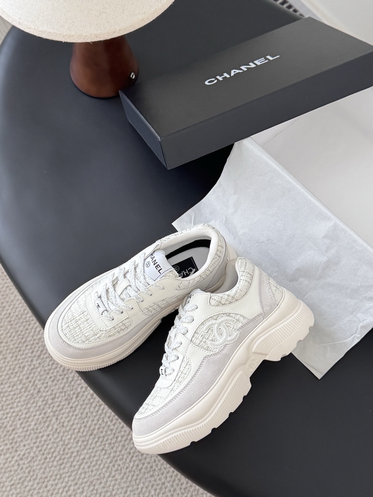 A pair of white Chanel sneakers featuring tweed panels and leather overlays presented next to an original black Chanel brand box. - Hình 4