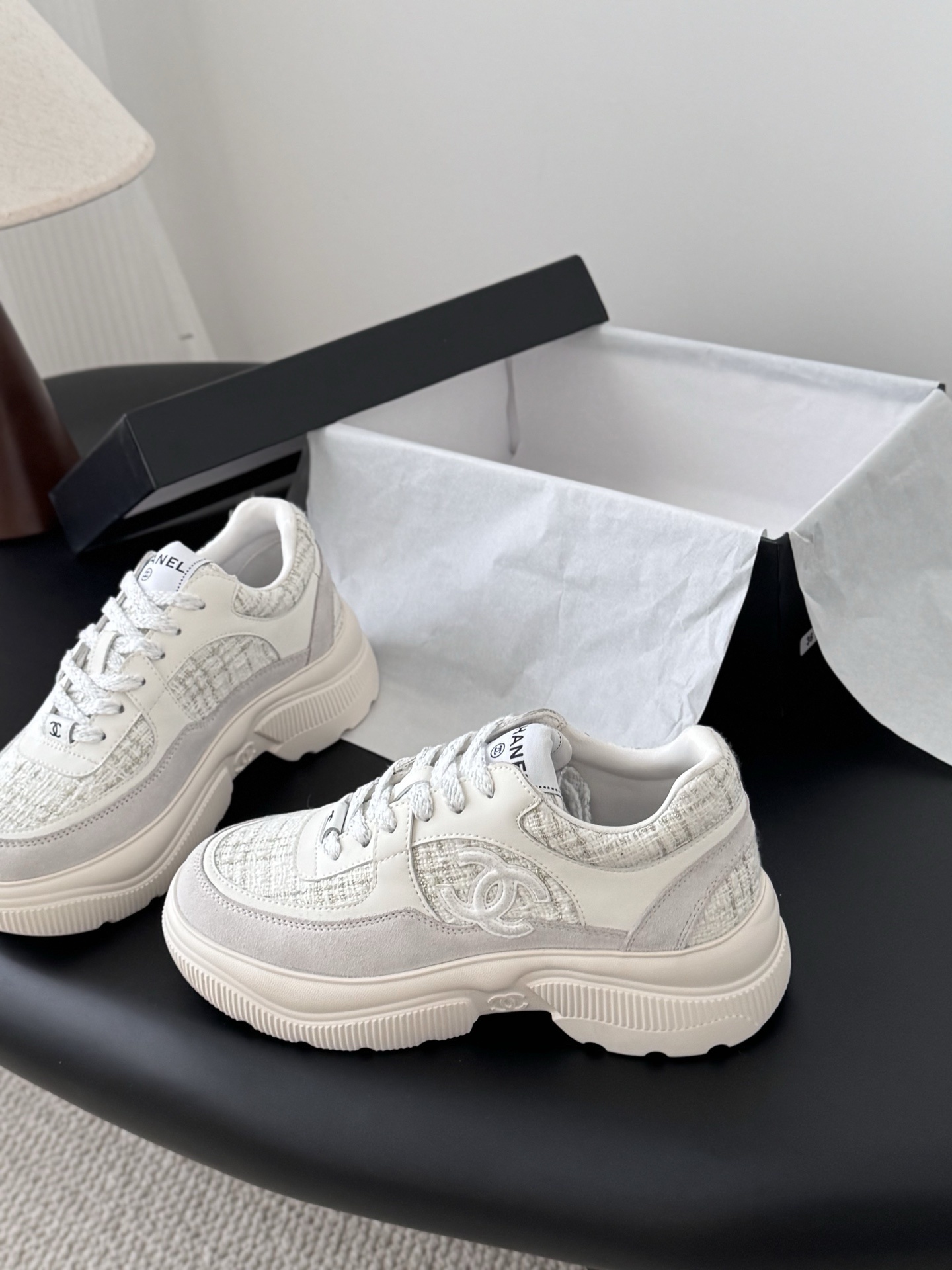 A pair of white Chanel sneakers featuring tweed panels and leather overlays presented next to an original black Chanel brand box. - Hình 2