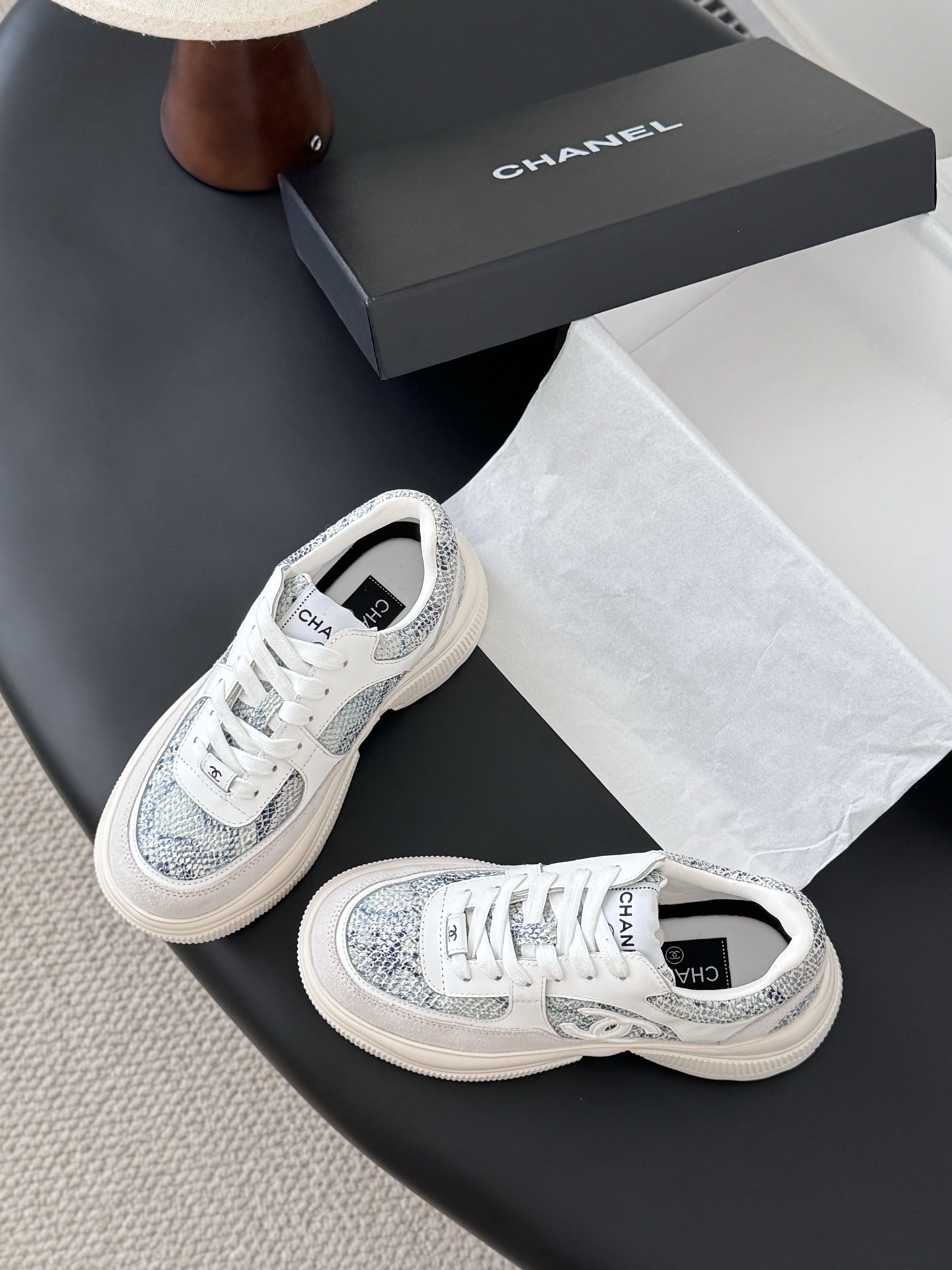 A pair of Chanel white chunky sneakers with blue snakeskin textured panels and the CC logo, displayed next to a black Chanel box. - Hình 6
