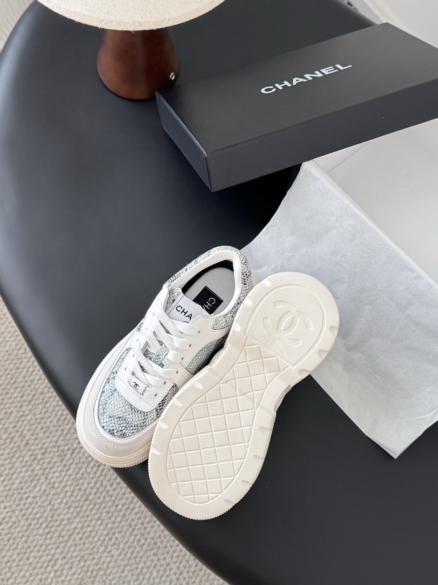 A pair of Chanel white chunky sneakers with blue snakeskin textured panels and the CC logo, displayed next to a black Chanel box. - Hình 5