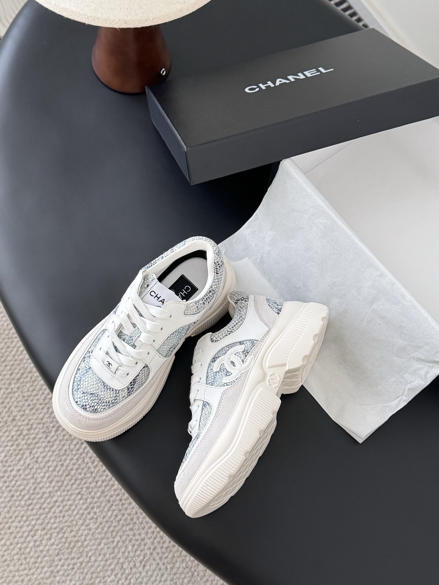 A pair of Chanel white chunky sneakers with blue snakeskin textured panels and the CC logo, displayed next to a black Chanel box. - Hình 4