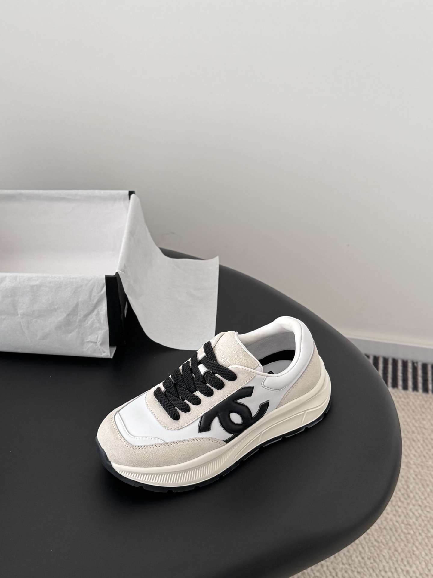 Pair of Chanel white and beige suede calfskin sneakers with black CC logo and black laces next to a branded box. - Hình 6