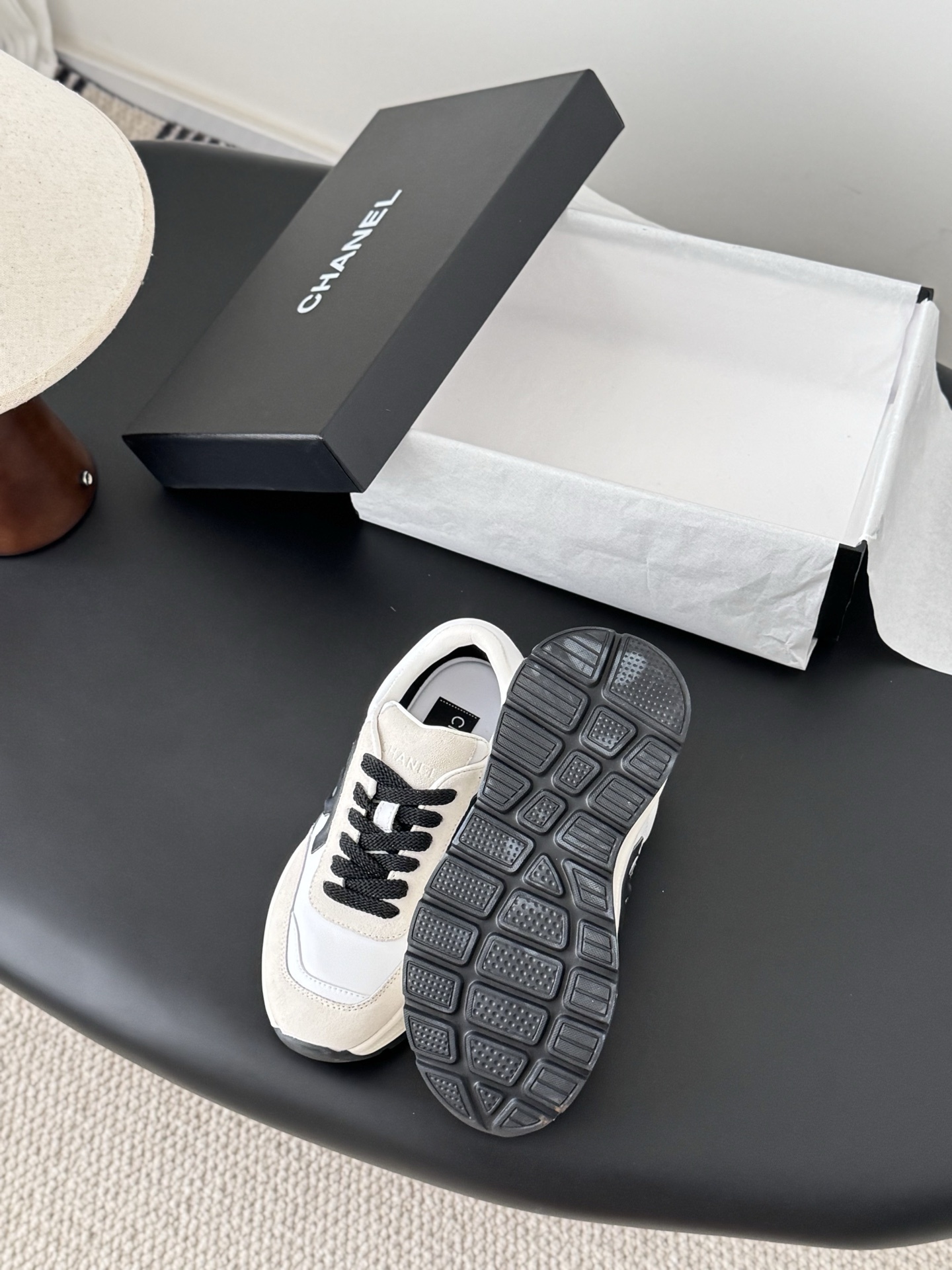 Pair of Chanel white and beige suede calfskin sneakers with black CC logo and black laces next to a branded box. - Hình 4