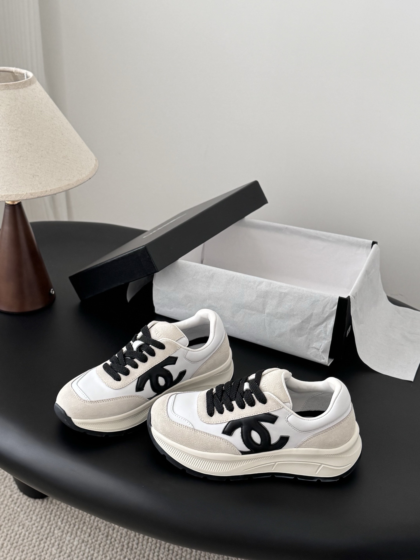 Pair of Chanel white and beige suede calfskin sneakers with black CC logo and black laces next to a branded box. - Hình 2