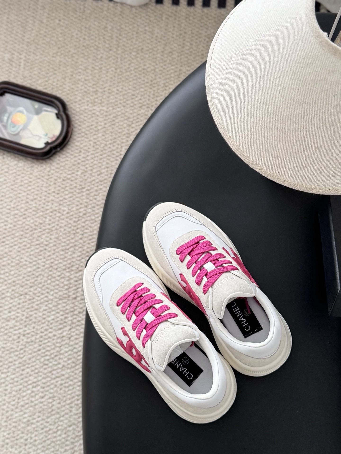 Pair of Chanel white and cream suede sneakers with hot pink laces and logo next to a black Chanel box - Hình 8