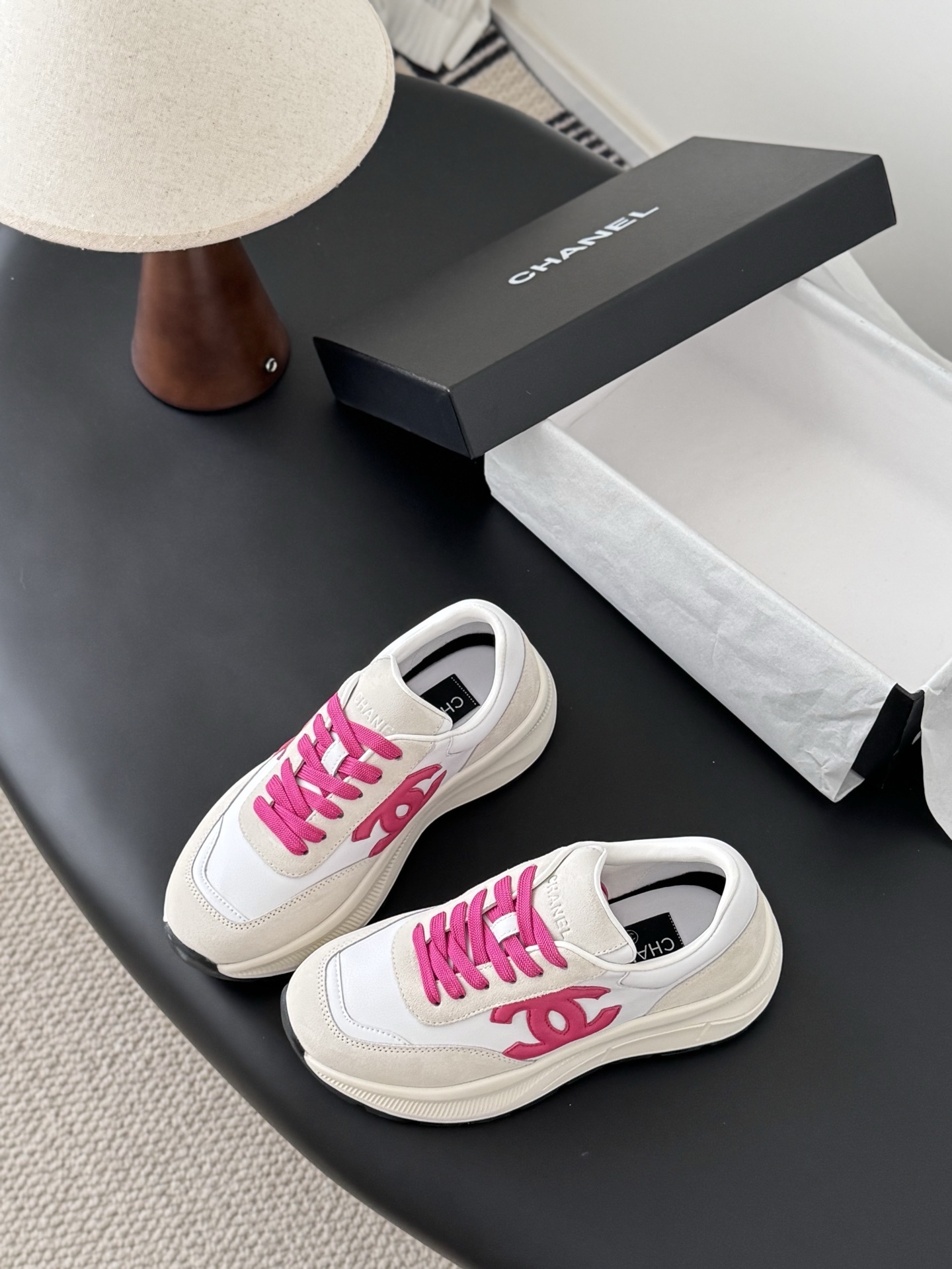 Pair of Chanel white and cream suede sneakers with hot pink laces and logo next to a black Chanel box - Hình 5