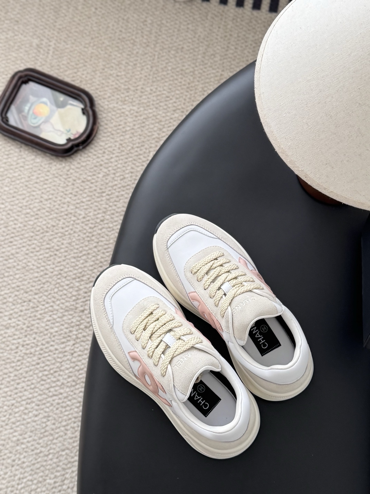 A pair of Chanel women's sneakers in white and beige suede with a pink CC logo, displayed next to a black Chanel shoe box. - Hình 8