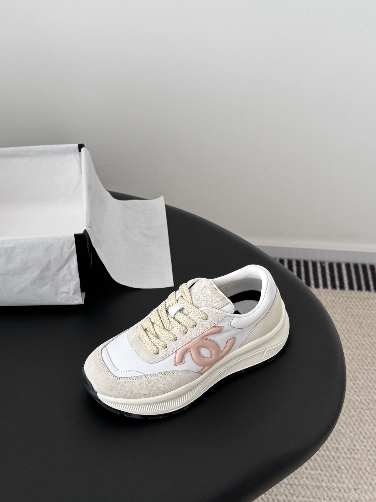 A pair of Chanel women's sneakers in white and beige suede with a pink CC logo, displayed next to a black Chanel shoe box. - Hình 6