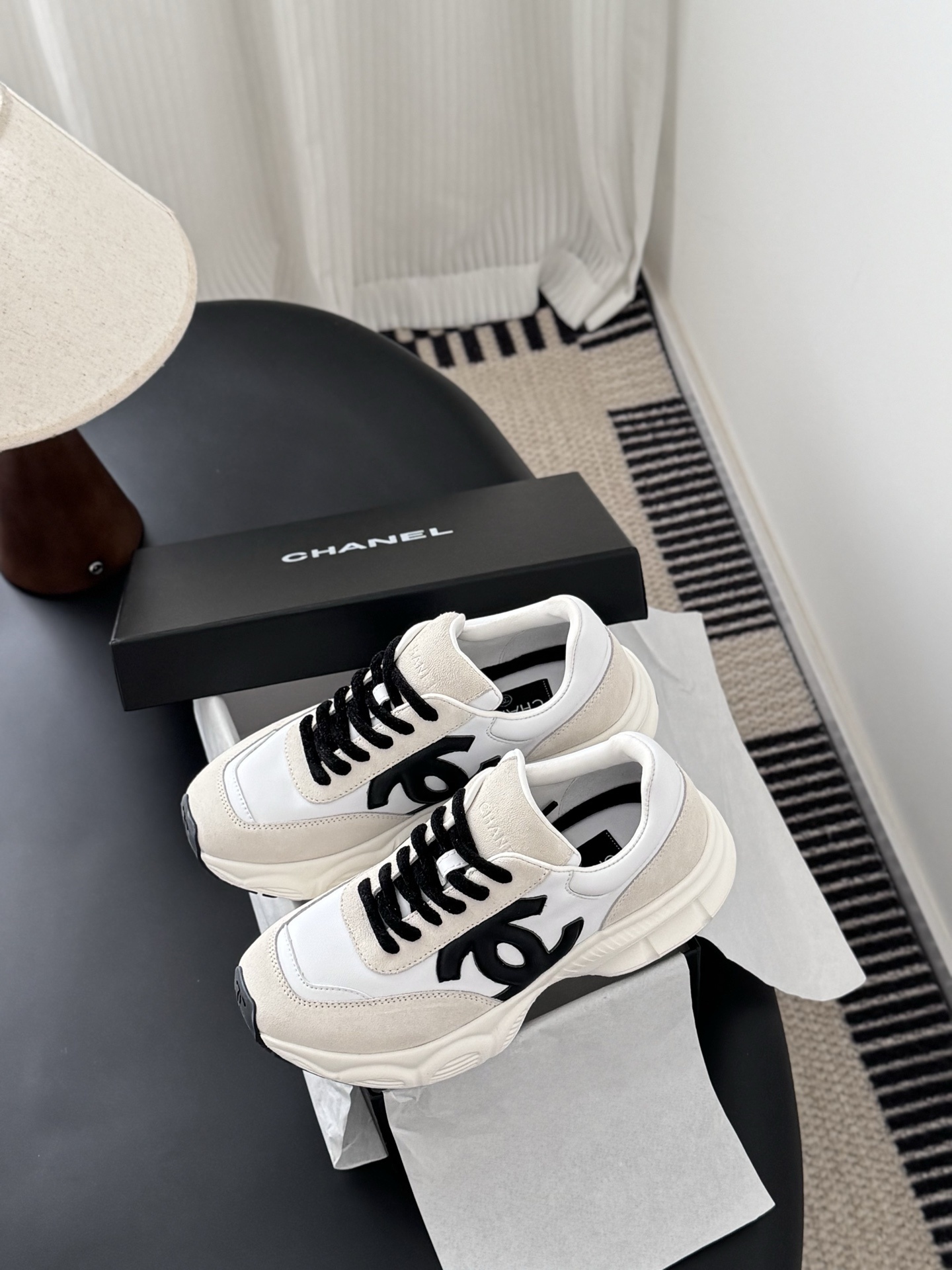 A pair of Chanel ivory and black suede leather sneakers with black CC logo and original black box on a table. - Hình 9