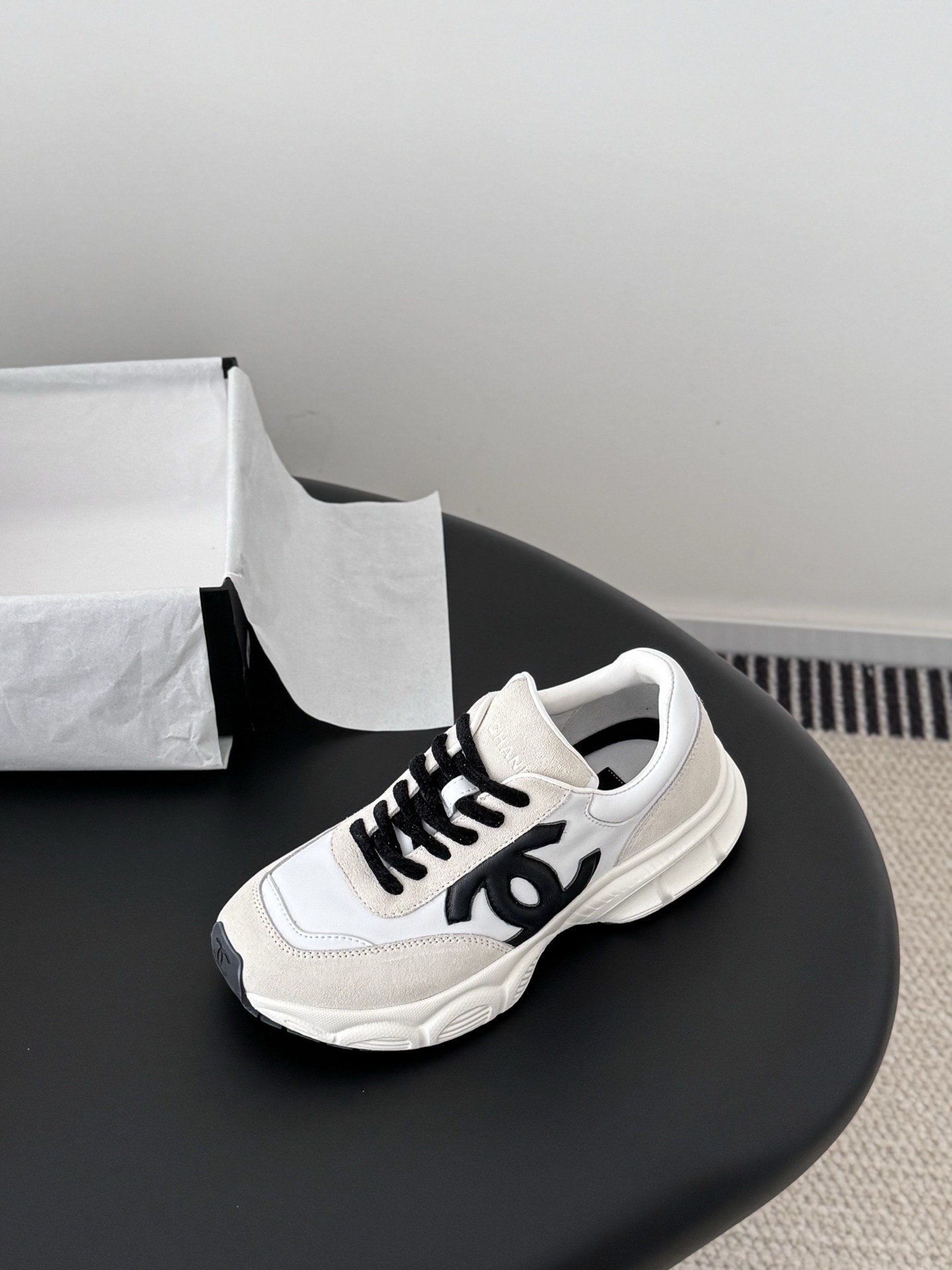 A pair of Chanel ivory and black suede leather sneakers with black CC logo and original black box on a table. - Hình 6
